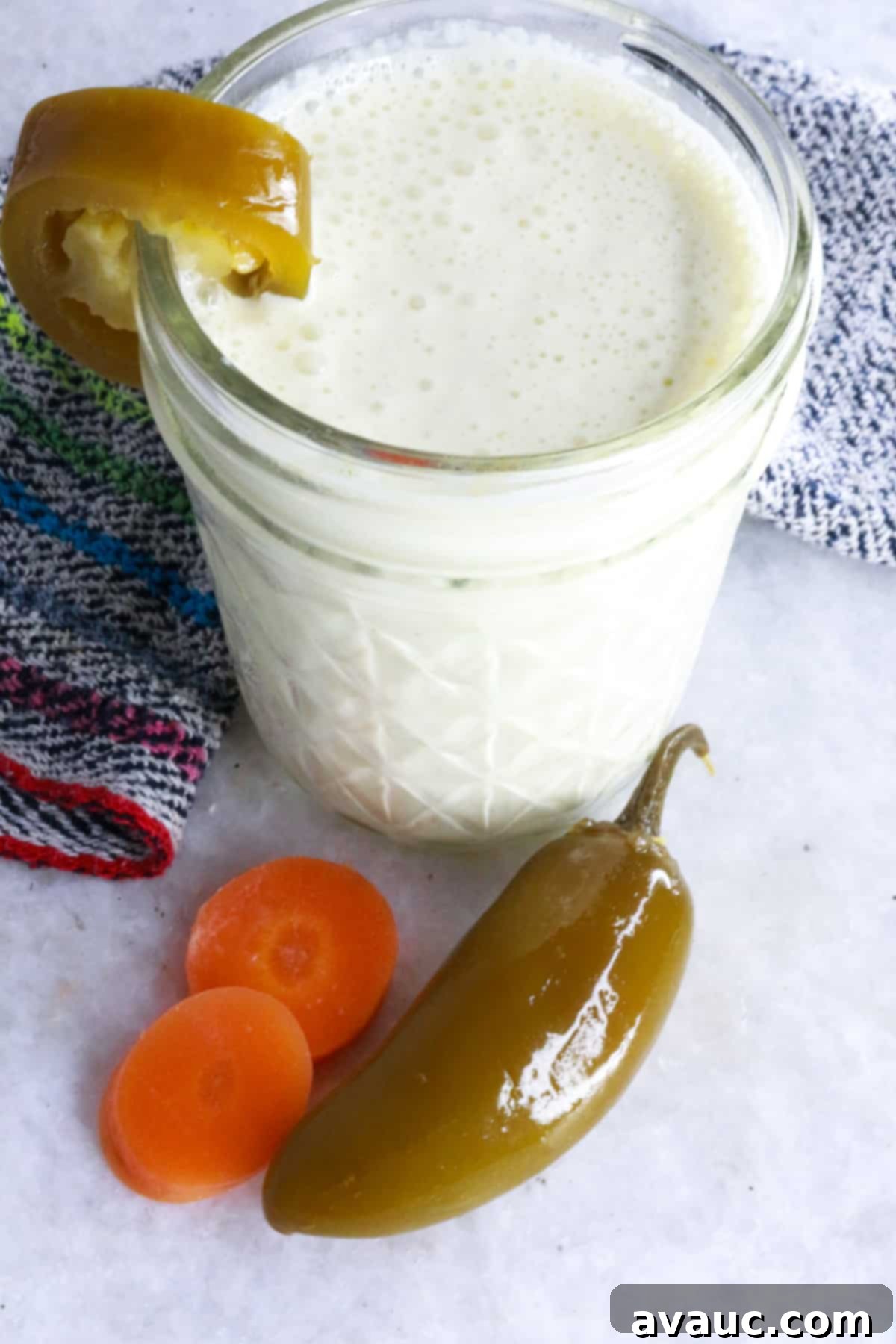 Jar of jalapeño sour cream garnished with a pickled jalapeño slice