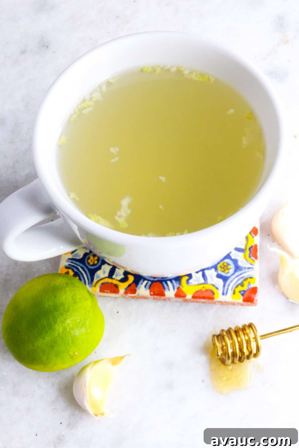 Homemade Garlic Tea Elixir 2 White mug with warm garlic tea on a coaster, surrounded by fresh lime slices and whole garlic cloves, emphasizing natural ingredients and a soothing remedy.