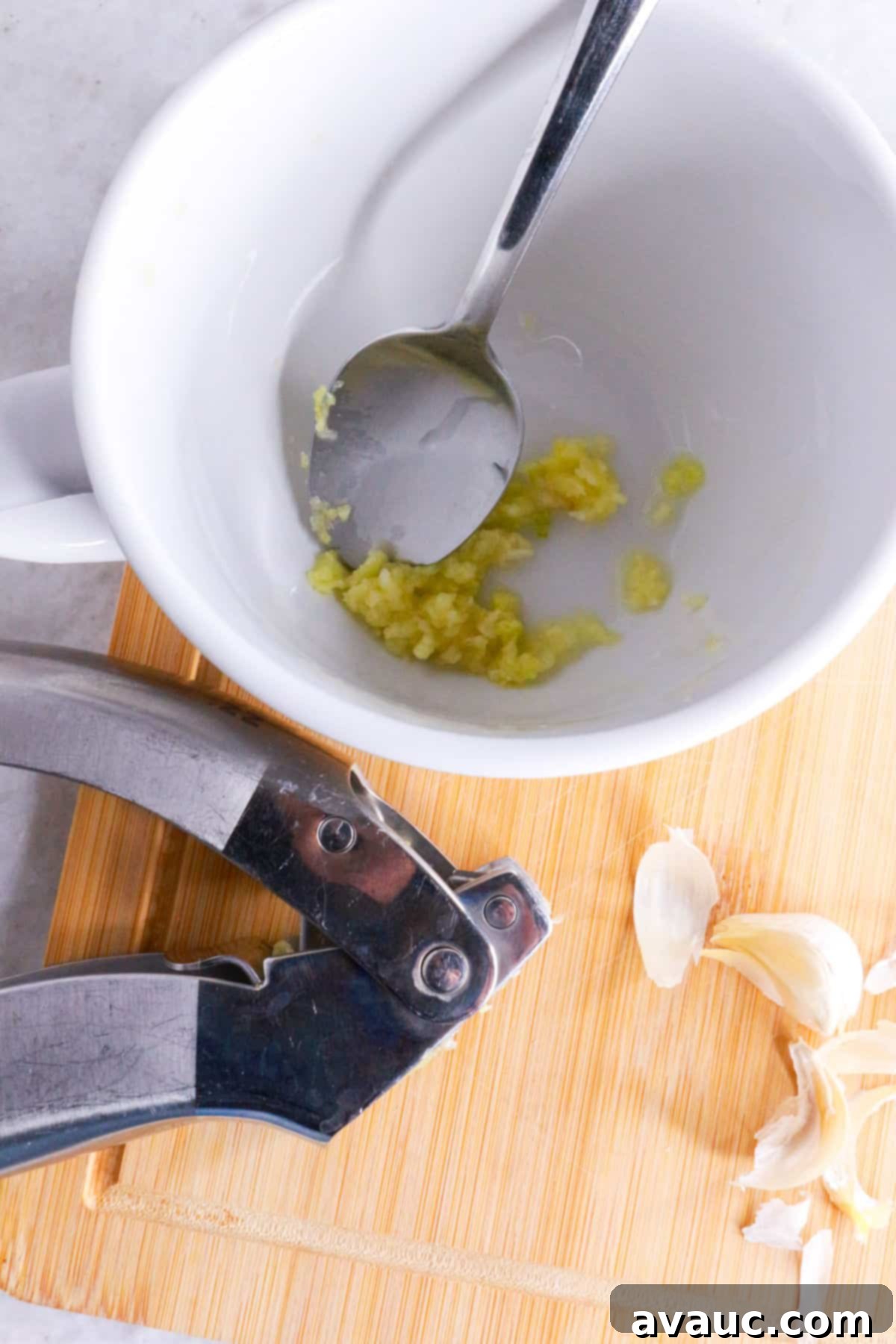 Homemade Garlic Tea Elixir 5 A white mug containing freshly crushed garlic, with a garlic press resting beside it on a wooden surface, ready for steeping.