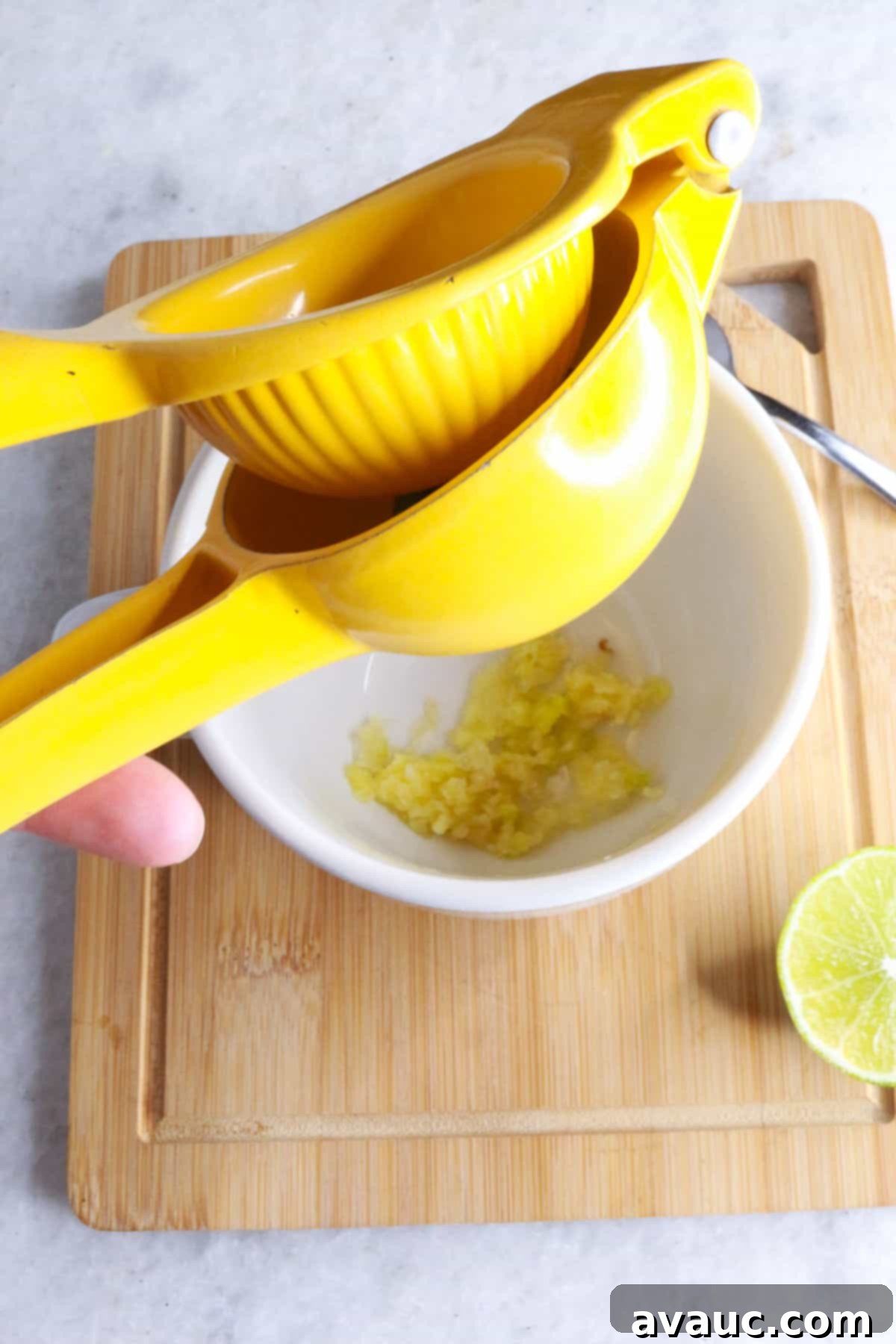 Homemade Garlic Tea Elixir 6 A hand squeezing fresh lime juice directly into a white mug already containing crushed garlic, preparing the tea base.