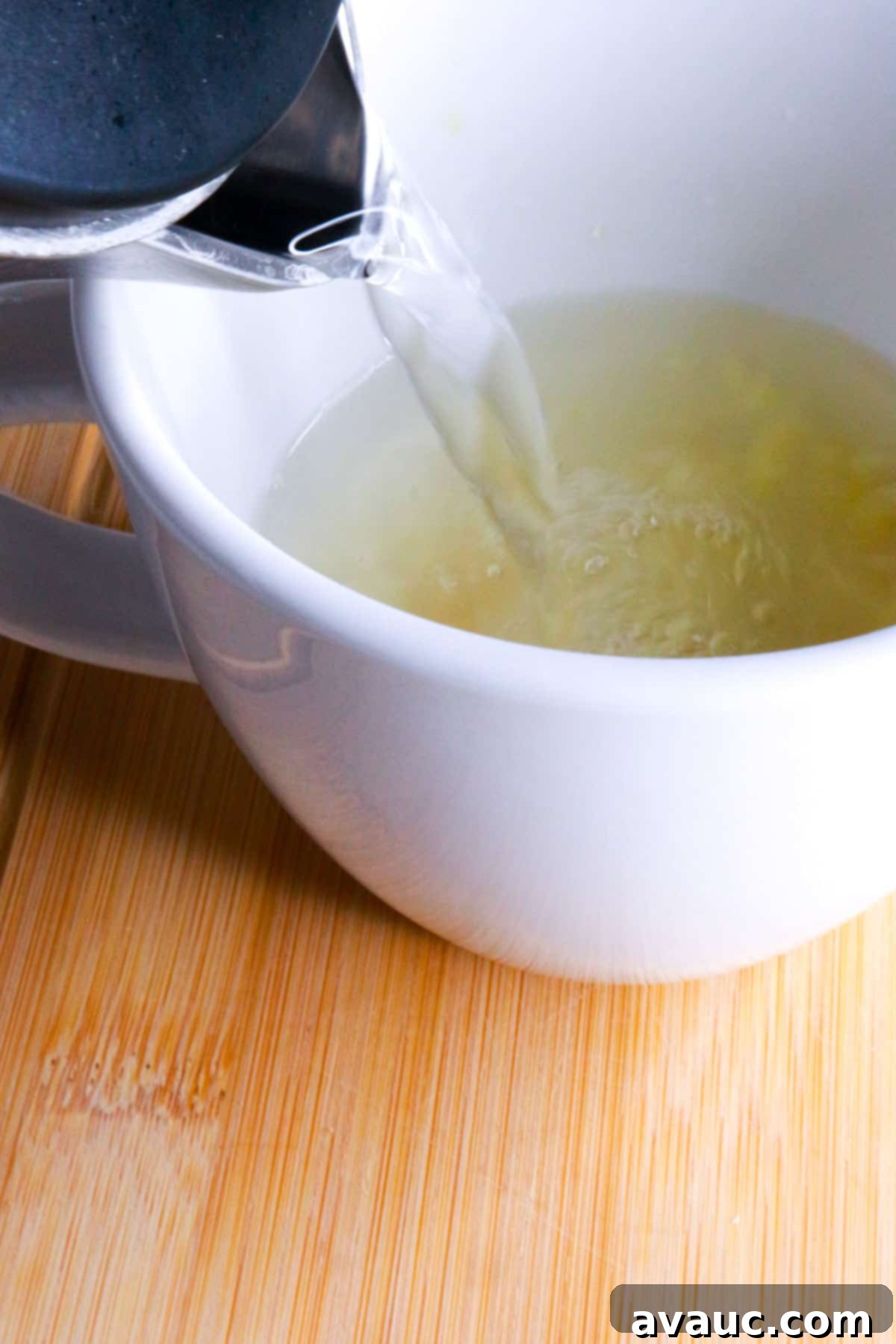 Homemade Garlic Tea Elixir 8 Hot water being carefully poured from a teapot into a white mug, where crushed garlic, honey, and lime are already waiting to steep into a health-boosting tea.