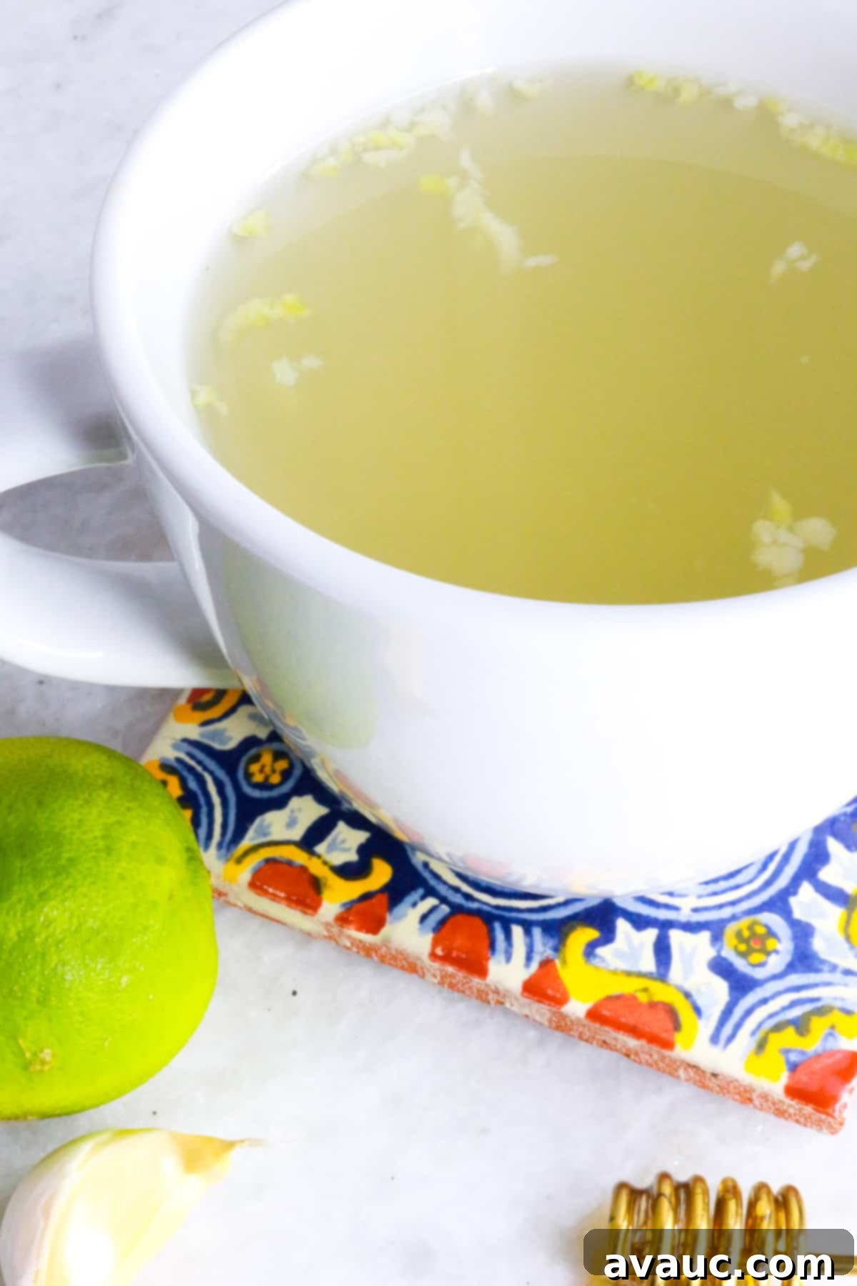 Homemade Garlic Tea Elixir 9 A beautifully composed final shot of a white mug of garlic tea on a wooden coaster, surrounded by fresh lime wedges and whole garlic cloves, ready to be enjoyed as a natural remedy.