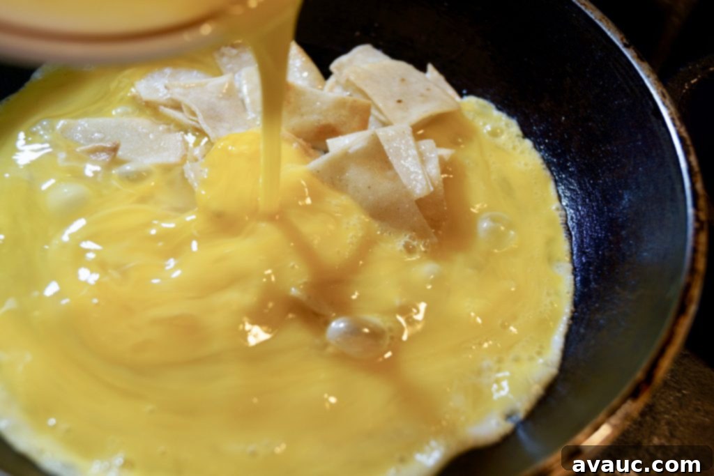 Scrambling eggs with fried tortillas in a pan for a delicious huevos con tortilla breakfast. #huevocontortillas #easybreakfast