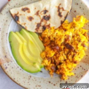 Plate with huevos con chorizo, corn tortilla and sliced avocado