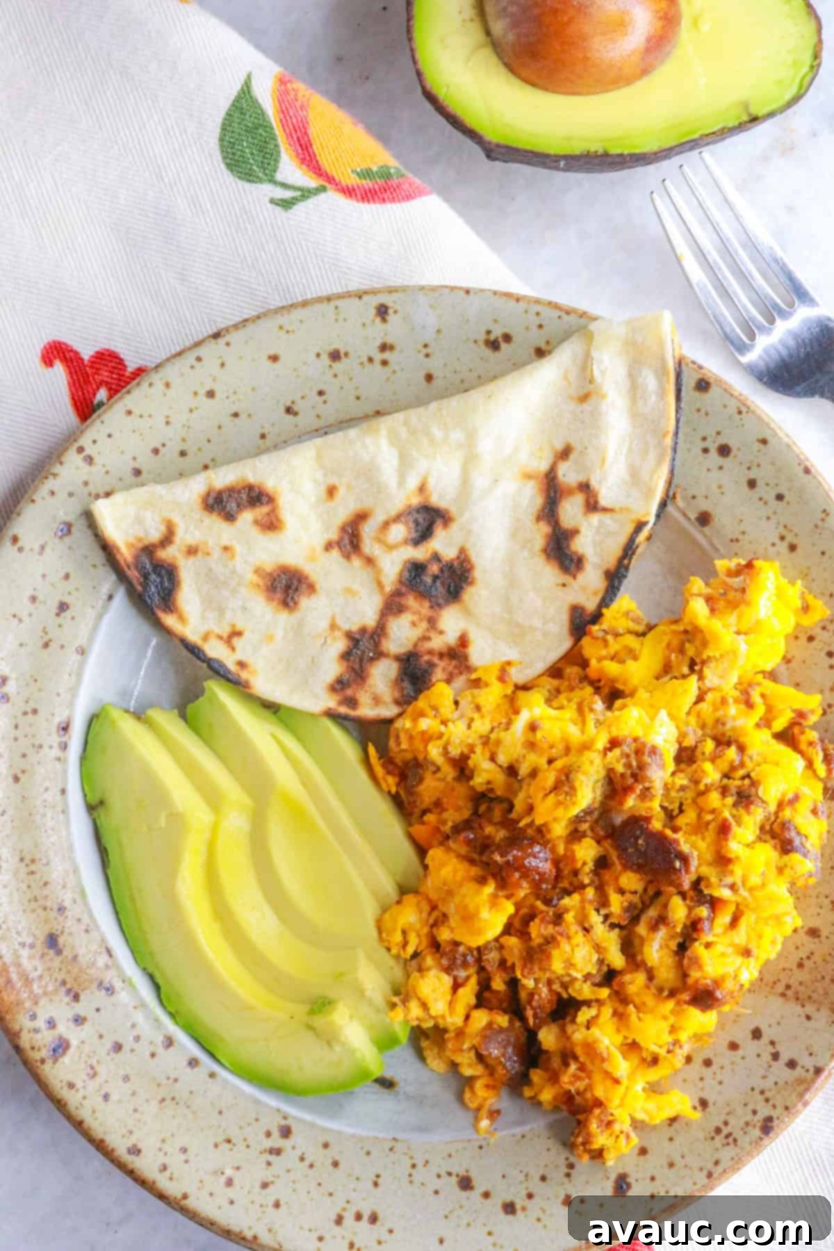 Plate with huevos con chorizo, corn tortilla and sliced avocado