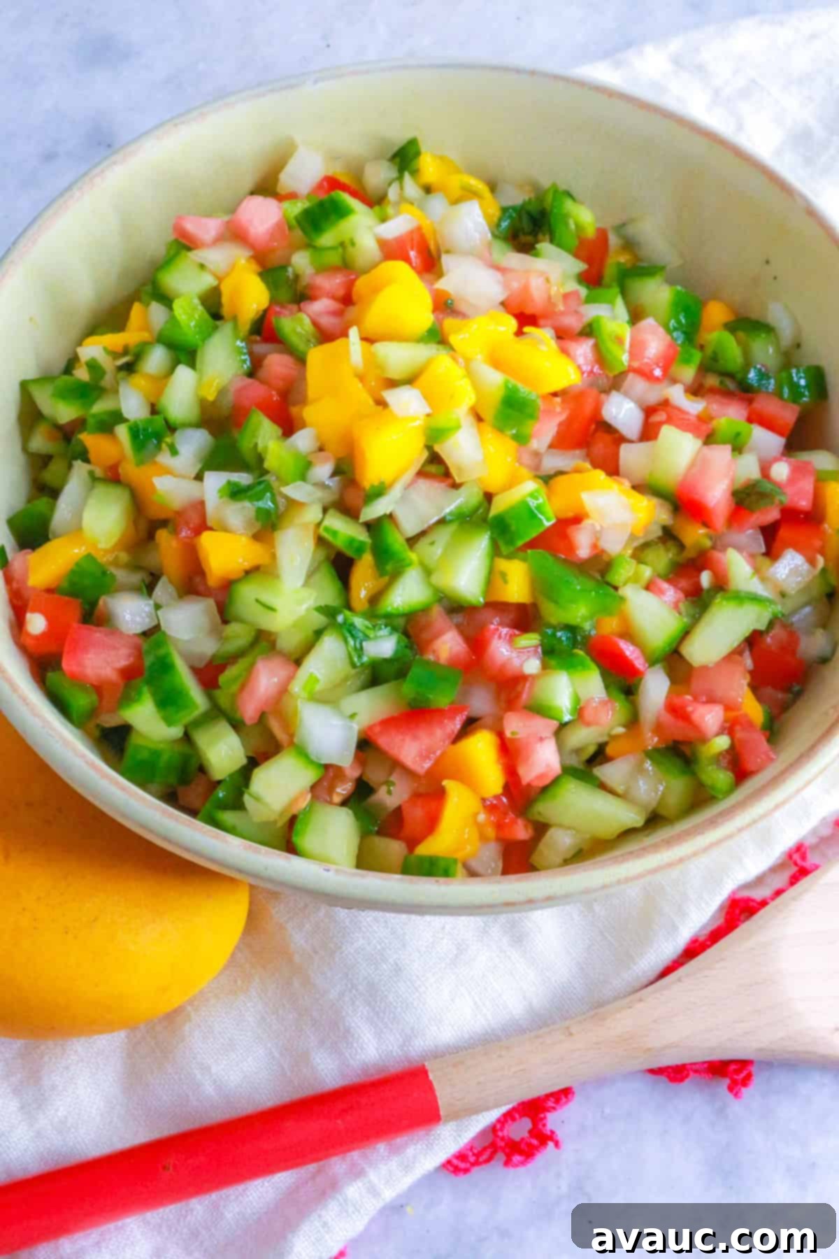 Mango pico de Gallo in a bowl with a mango and wooden spoon by it