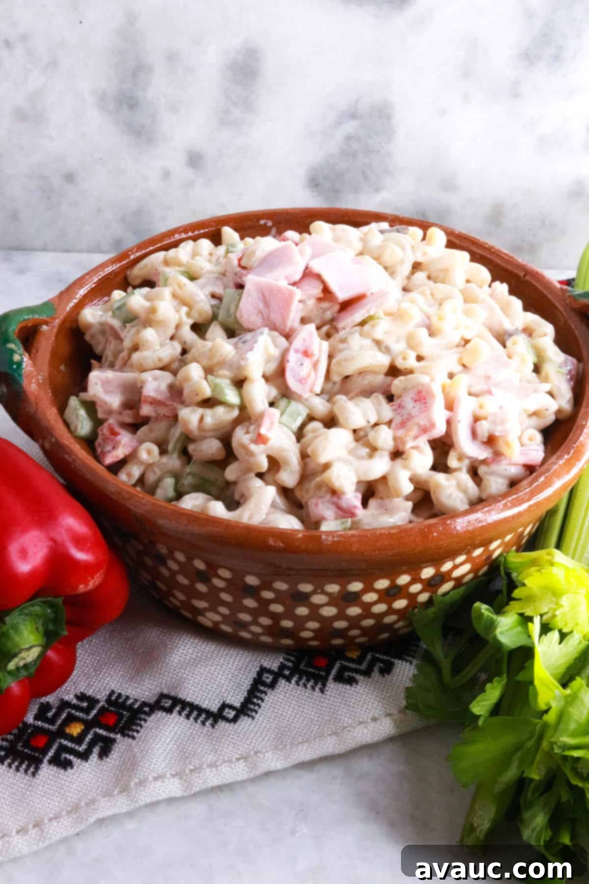 Ensalada de Coditos in a brown bowl with a red bell pepper and stalk of celery beside it.