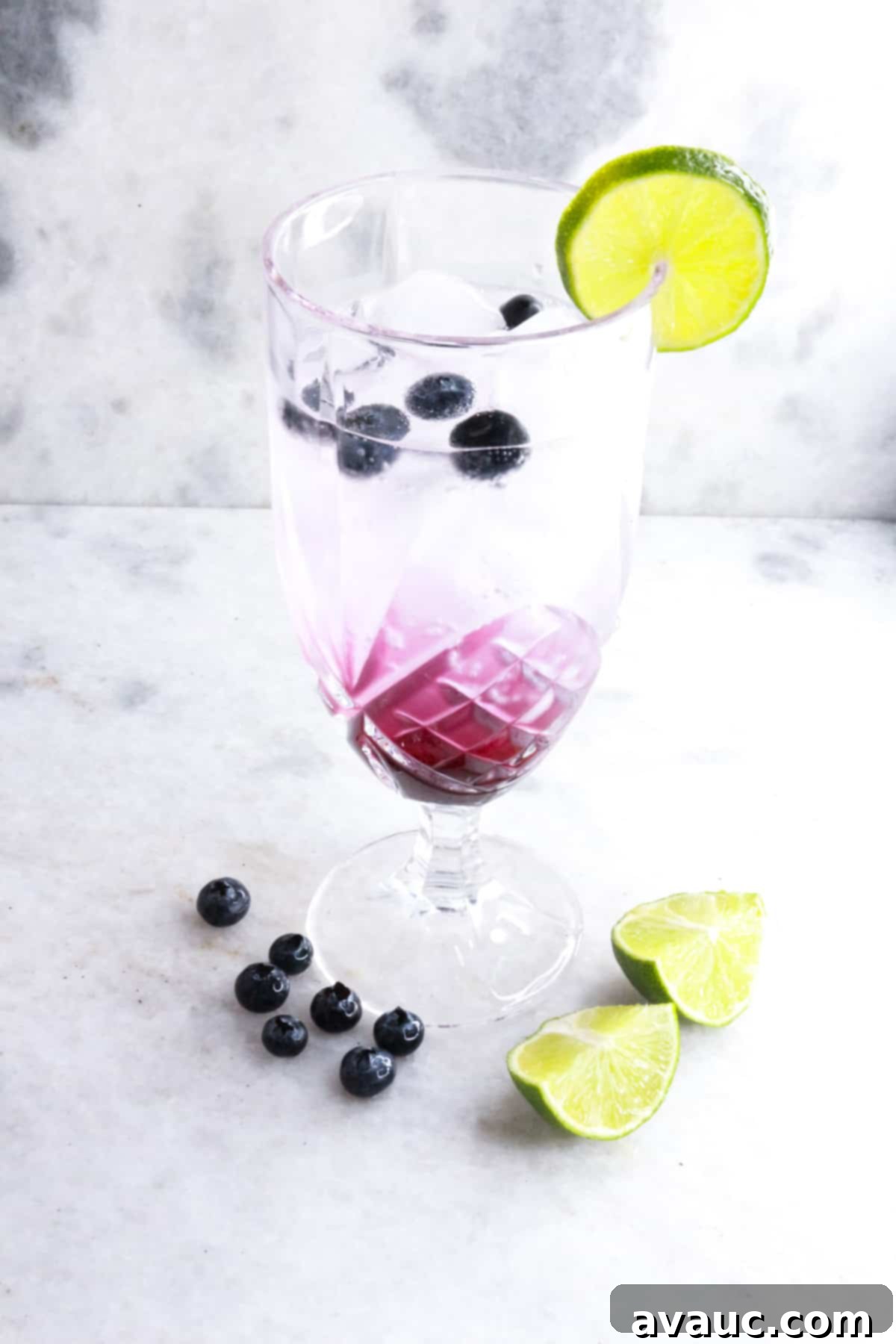 Vibrant Berry Refresher 2 Tall glass with vibrant purple blueberry mocktail garnished with fresh blueberries and a slice of lime