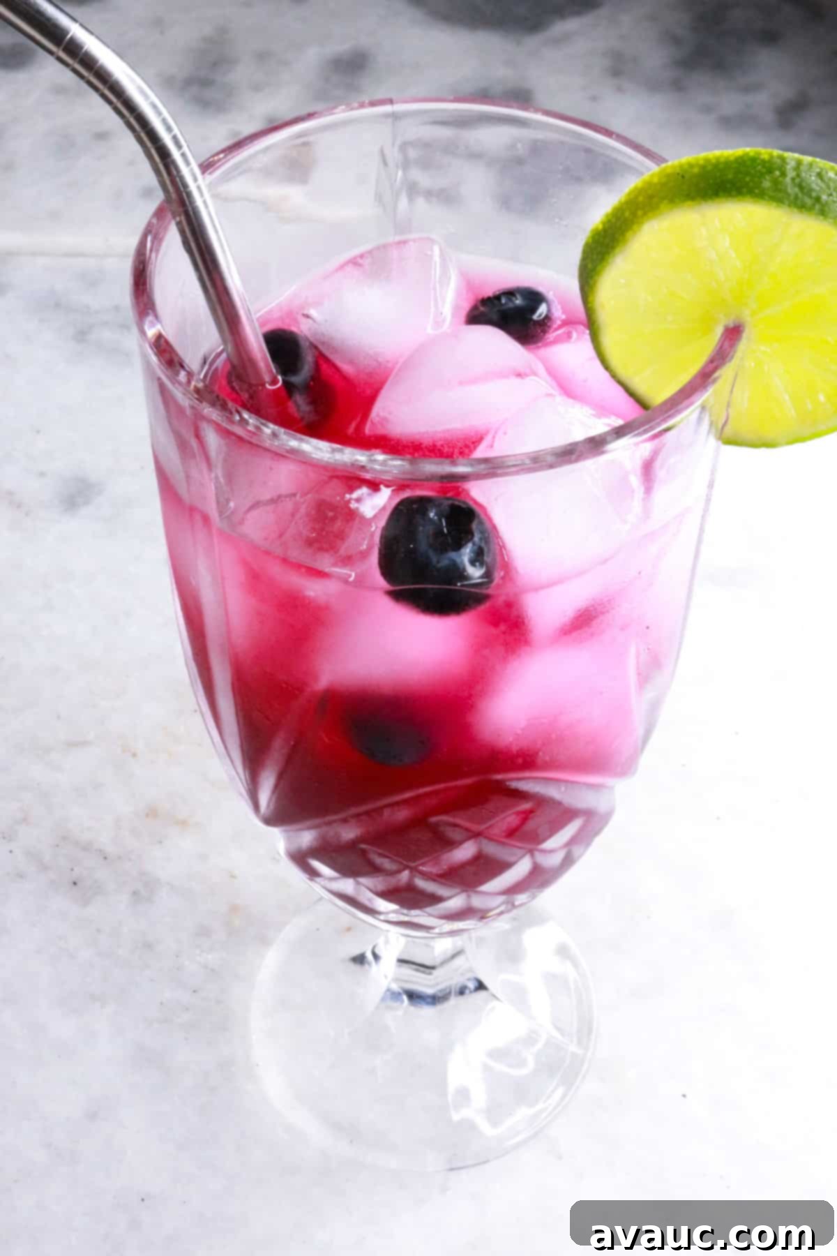 Vibrant Berry Refresher 11 Tall glass with vibrant purple blueberry mocktail mixed with a straw, garnished with fresh blueberries.