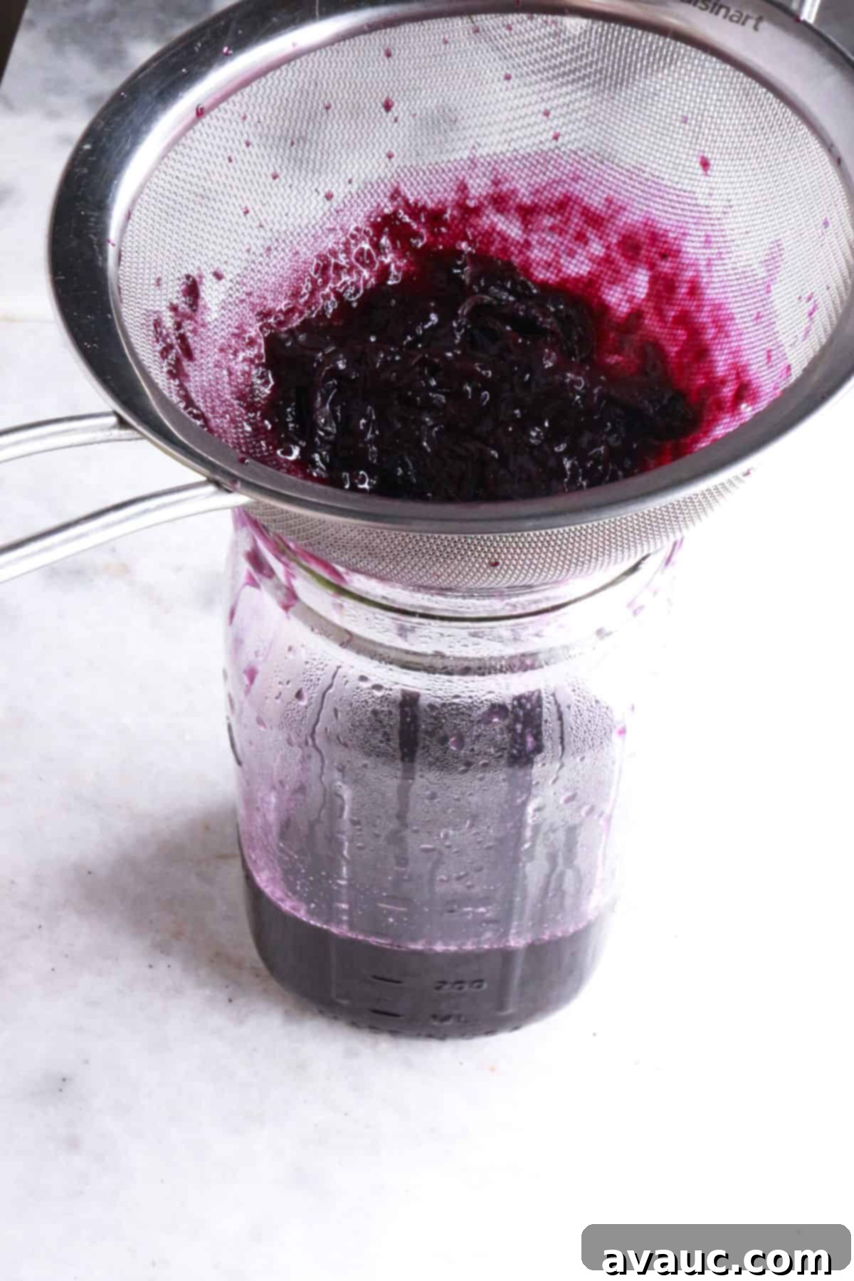 Vibrant Berry Refresher 6 Straining the cooled blueberry simple syrup through a fine mesh sieve into a glass jar for storage.