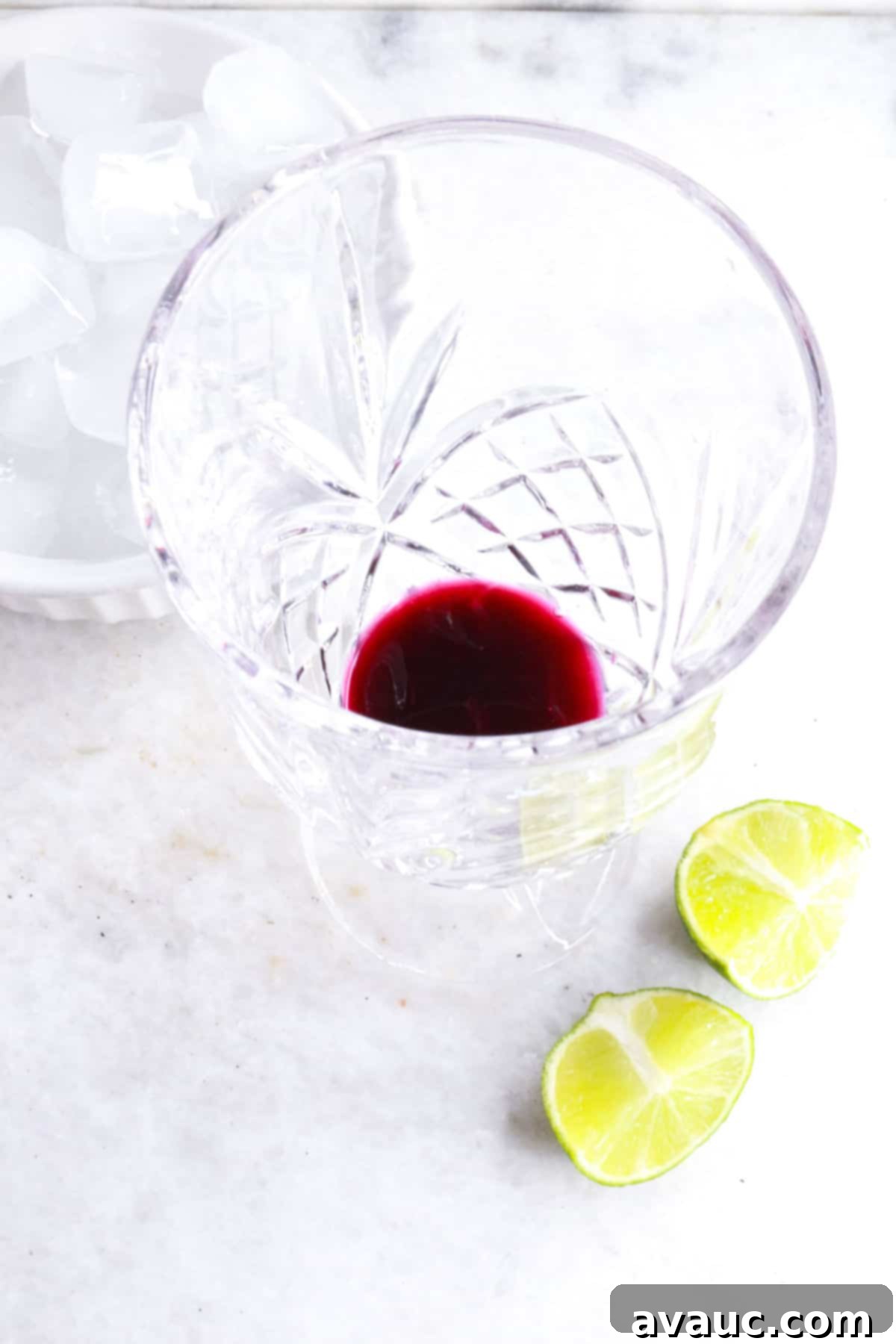 Vibrant Berry Refresher 7 Glass with blueberry simple syrup at the bottom, alongside a bowl of ice and fresh lime wedges.