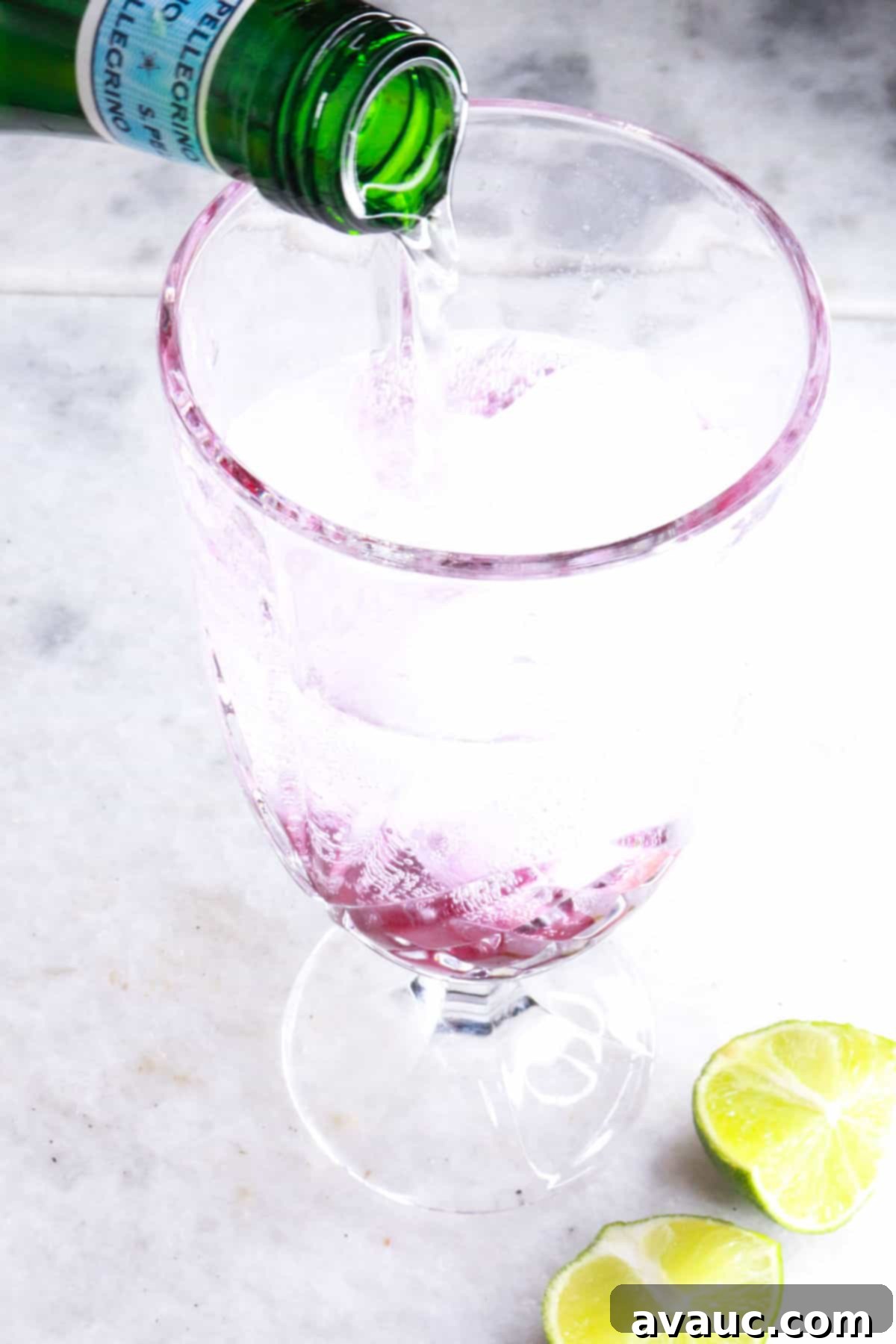 Vibrant Berry Refresher 9 Pouring sparkling water into a tall glass containing ice and blueberry honey simple syrup, creating a bubbly mocktail.