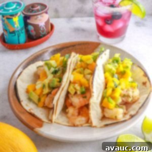 Zesty Shrimp Tacos with Tropical Mango Salsa 12 A plate with three shrimp tacos with mango salsa and a sparkling blueberry mocktail behind it