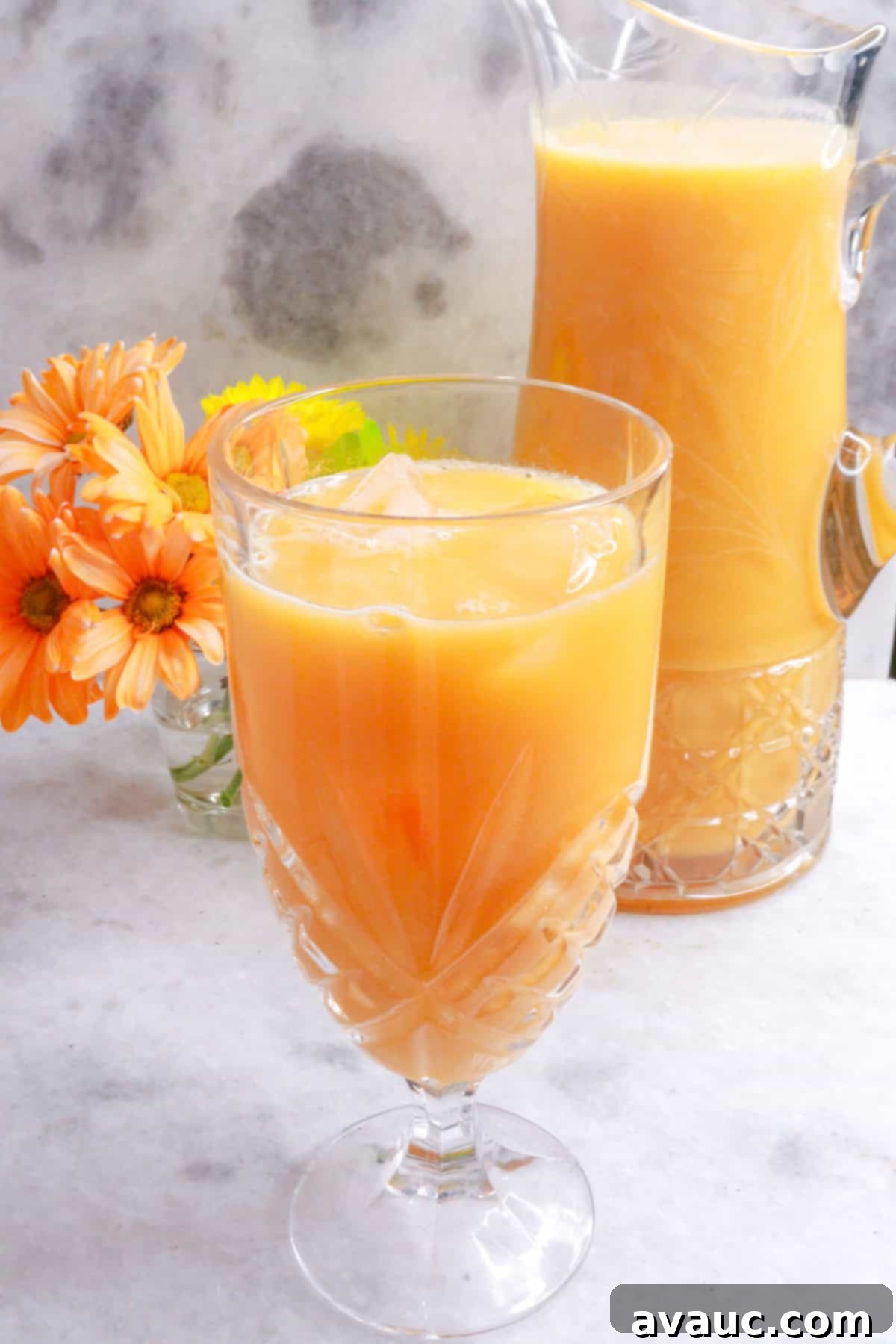 Mexican Melon Refresher 2 Agua de Melón in a glass with a pitcher and flowers behind it