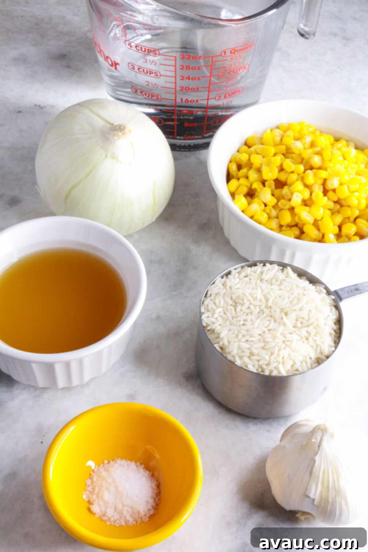 Zesty Mexican White Rice with Sweet Corn 3 Collection of fresh ingredients for Mexican white rice with corn: water in measuring cup, bowl of corn, an onion, broth, rice, salt, and garlic bulb