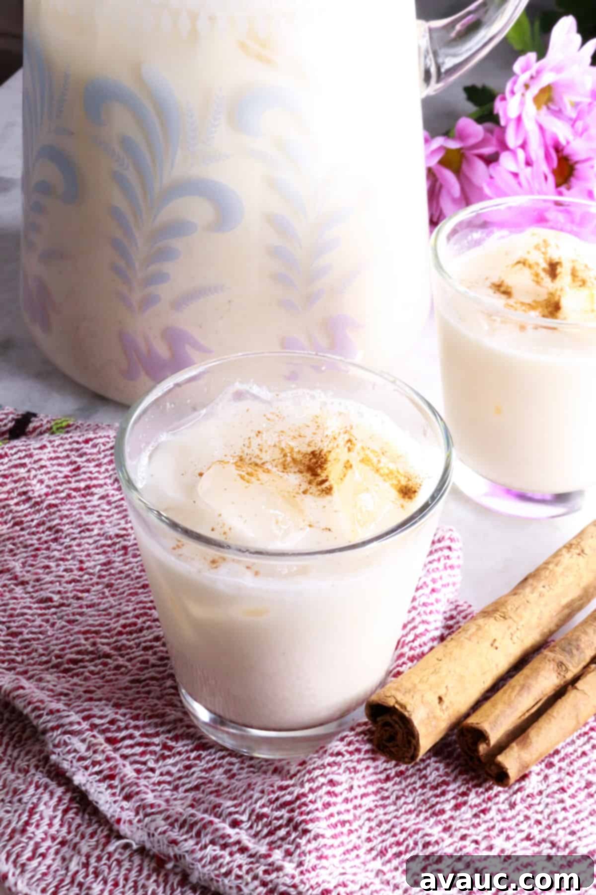 Cooling Horchata Delight 2 A glass pitcher and two glasses filled with Horchata Agua Fresca, garnished with cinnamon sticks and a sprinkle of ground cinnamon.