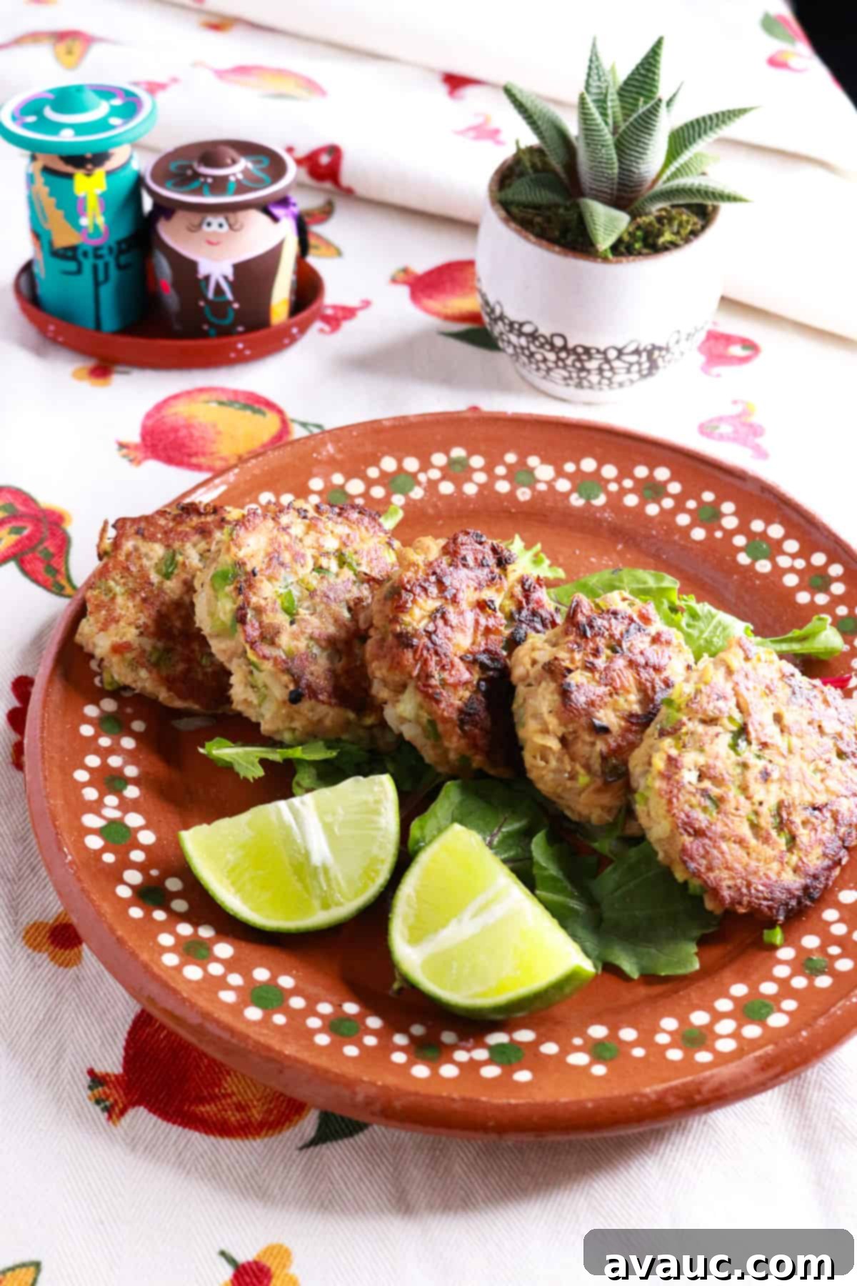 Mexican Tuna Croquettes 8 Mexican tuna cakes on a plate on top of greens and beside lime wedges.