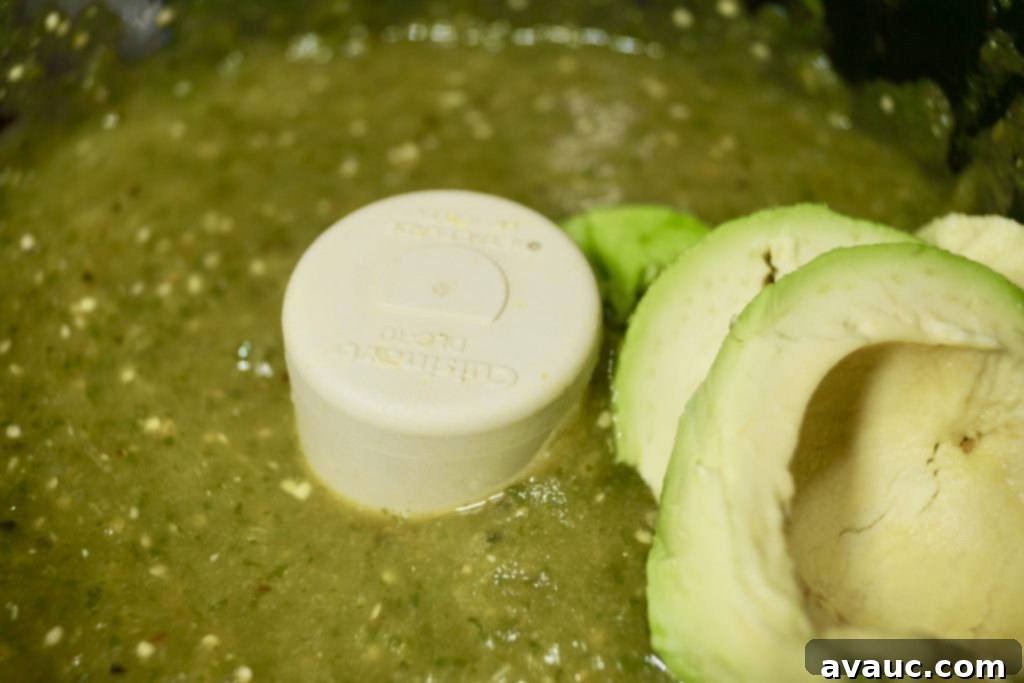 Adding ripe avocado to the blended tomatillo salsa for a creamy texture