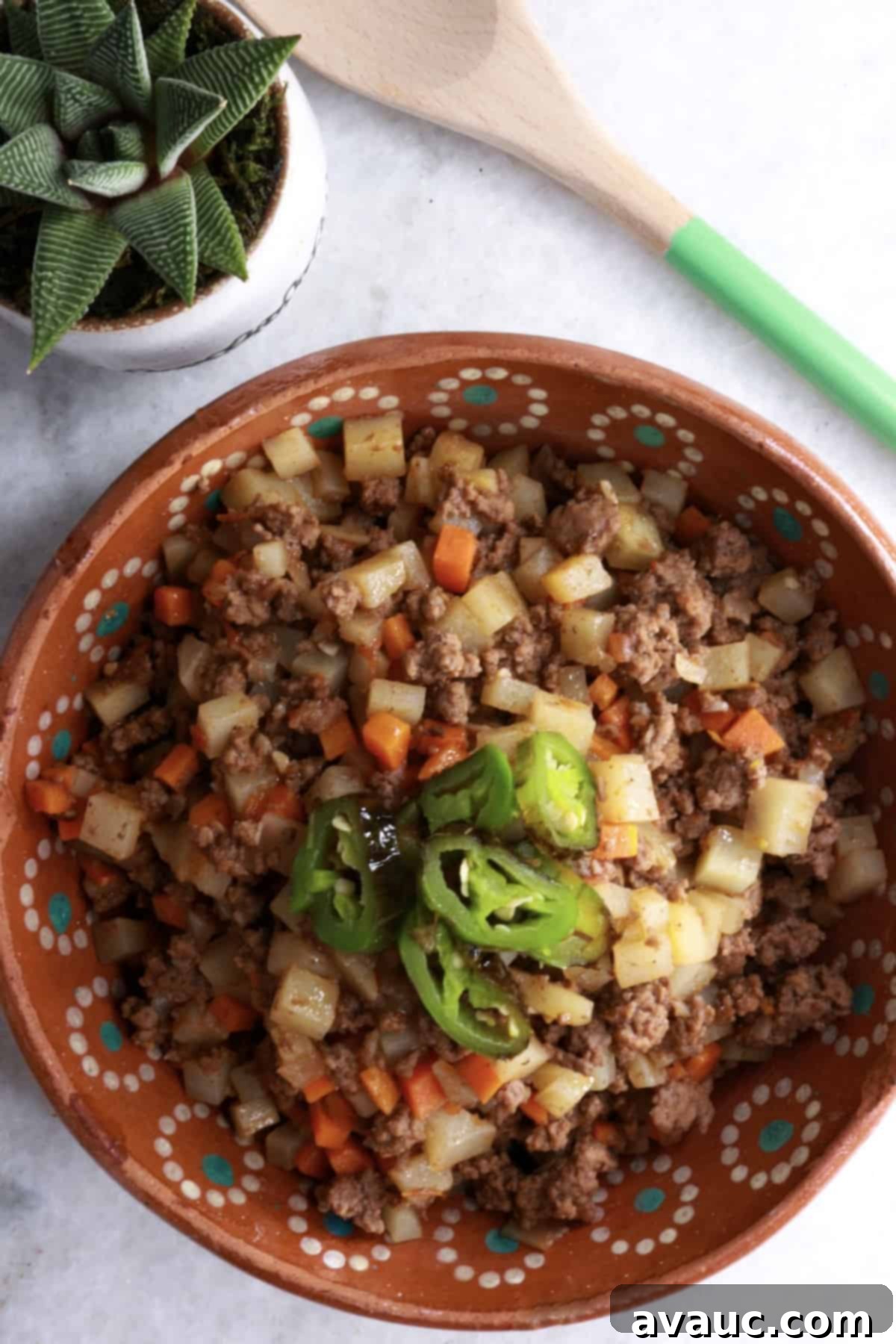 Bowl of picadillo con papas topped with sliced jalapeños, ready to be served