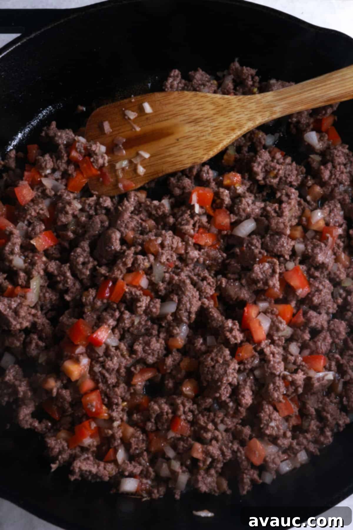 Ground beef cooking in a skillet with diced onion, tomato, and garlic.