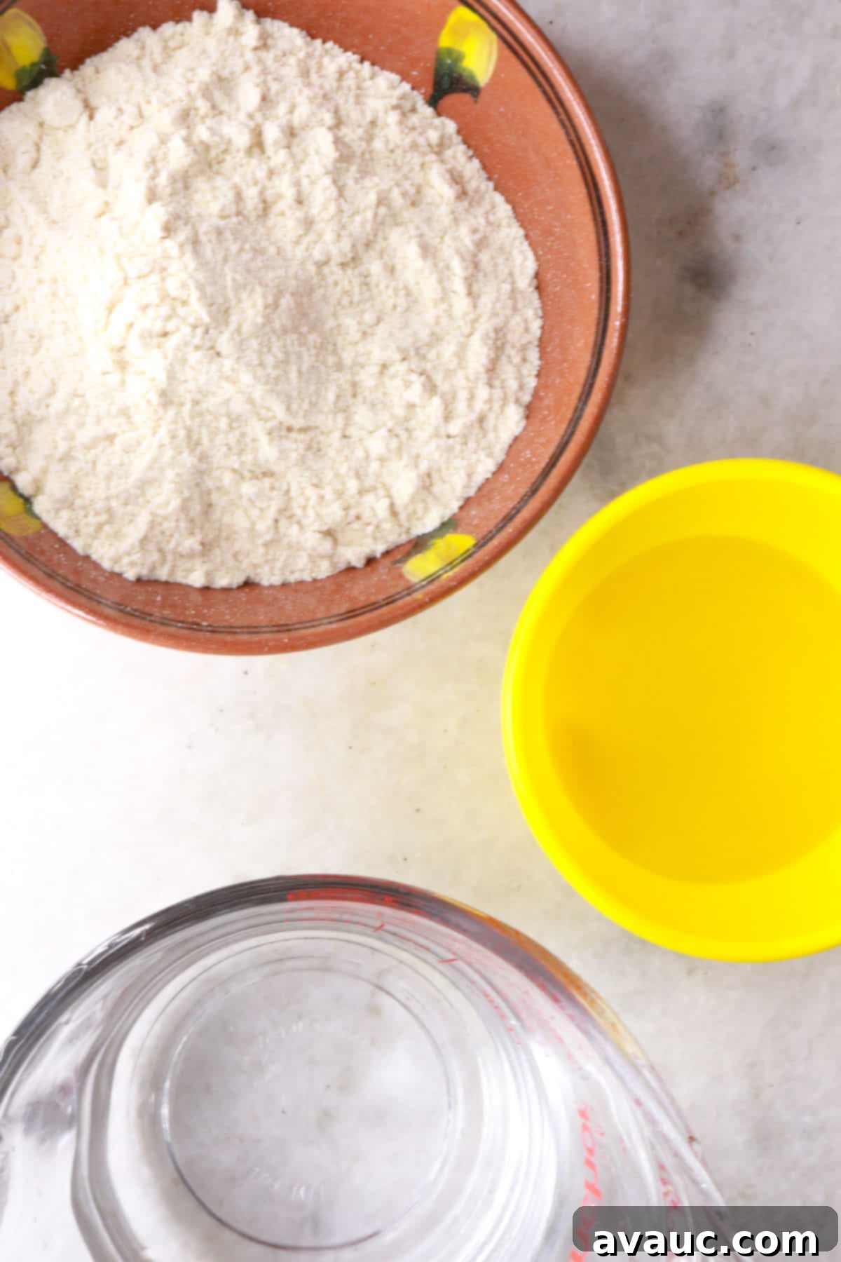 Key ingredients for a Sopes recipe laid out: masa harina in a bowl, a bottle of oil, and a glass of water