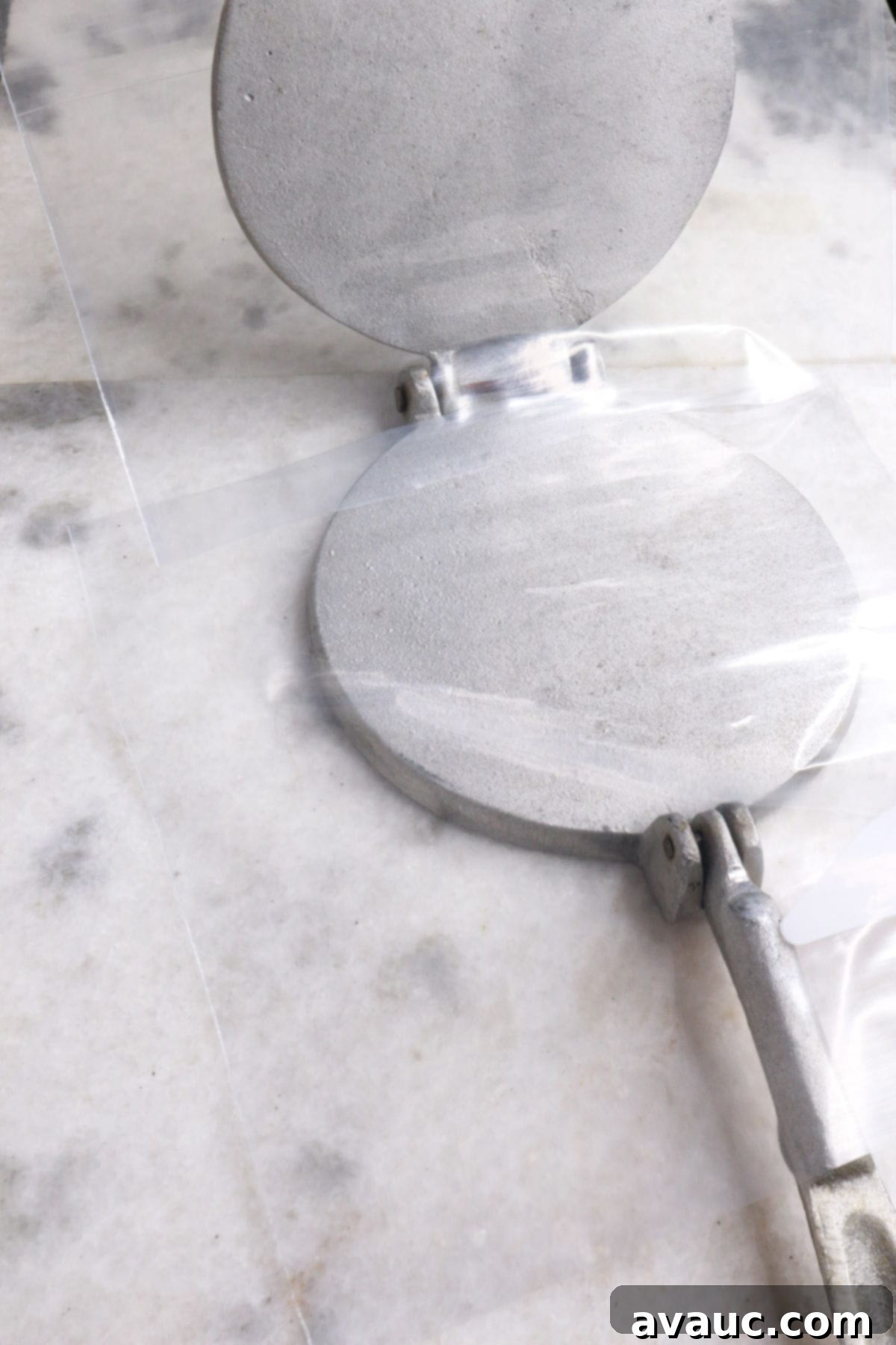An open tortilla press with two square sheets of plastic from a ziplock bag, ready for dough