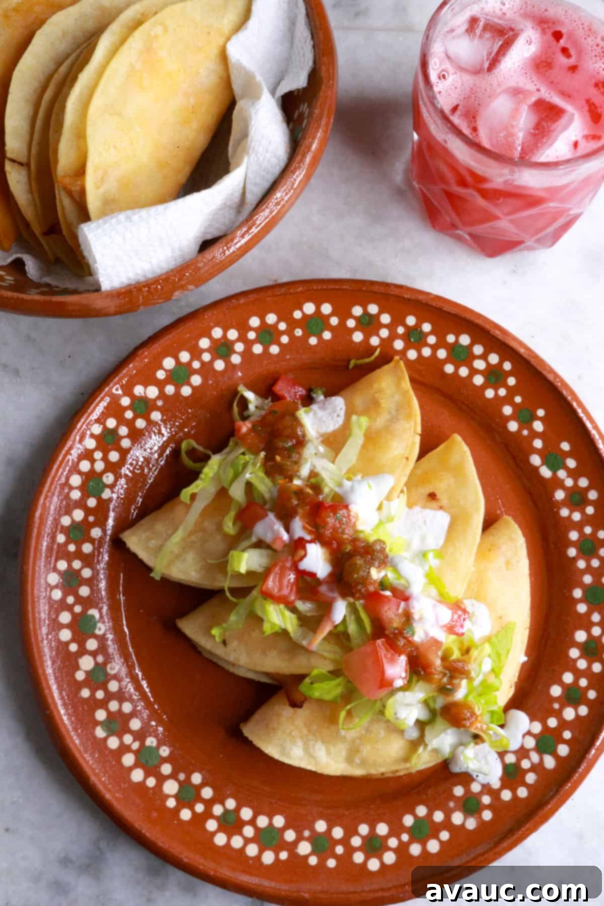 Crunchy Golden Chicken Tacos 2 Three tacos dorados de pollo on a brown Mexican plate topped with garnishes like shredded lettuce, diced tomatoes, and a dollop of sour cream, showcasing their golden crispness