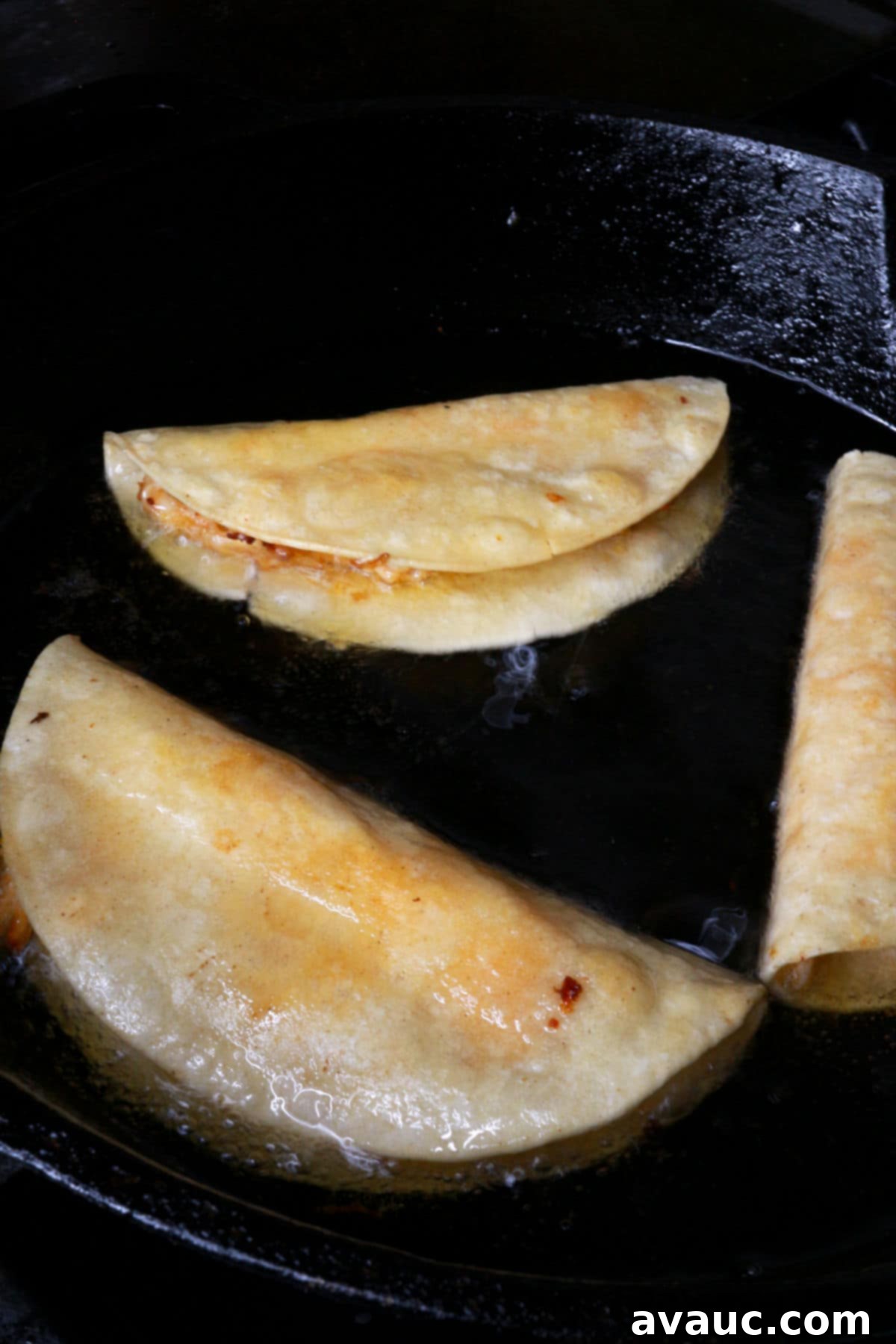 Crunchy Golden Chicken Tacos 11 Three chicken tacos dorados frying in hot oil within a cast-iron skillet, turning a beautiful golden brown