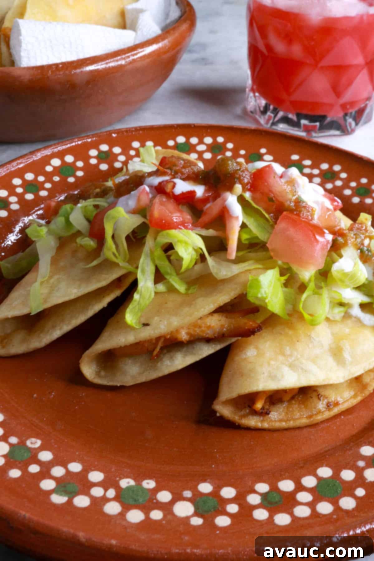 Crunchy Golden Chicken Tacos 12 Three crispy chicken tacos on a rustic brown Mexican plate, generously topped with shredded lettuce, diced tomatoes, a drizzle of sour cream, and a hint of salsa, beautifully presented