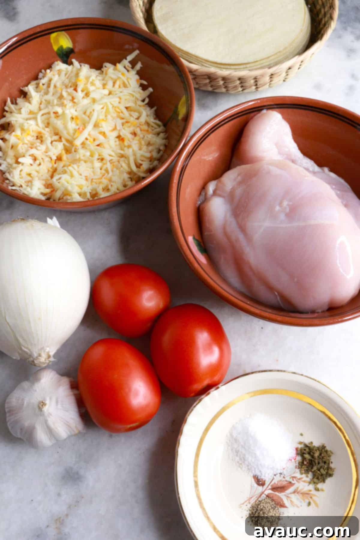 Crunchy Golden Chicken Tacos 3 A collection of fresh ingredients for tacos dorados de pollo, including corn tortillas, shredded cheese, raw chicken breasts, Roma tomatoes, an onion, a garlic bulb, and a bowl of spices, arranged on a rustic wooden background