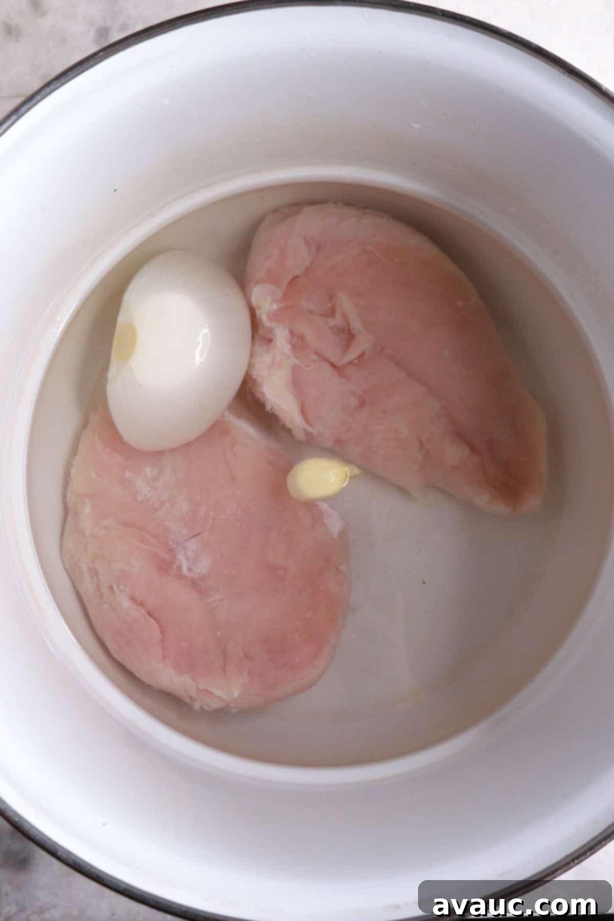 Crunchy Golden Chicken Tacos 4 A medium pot containing two raw chicken breasts, a piece of onion, and a garlic clove submerged in water, ready for cooking