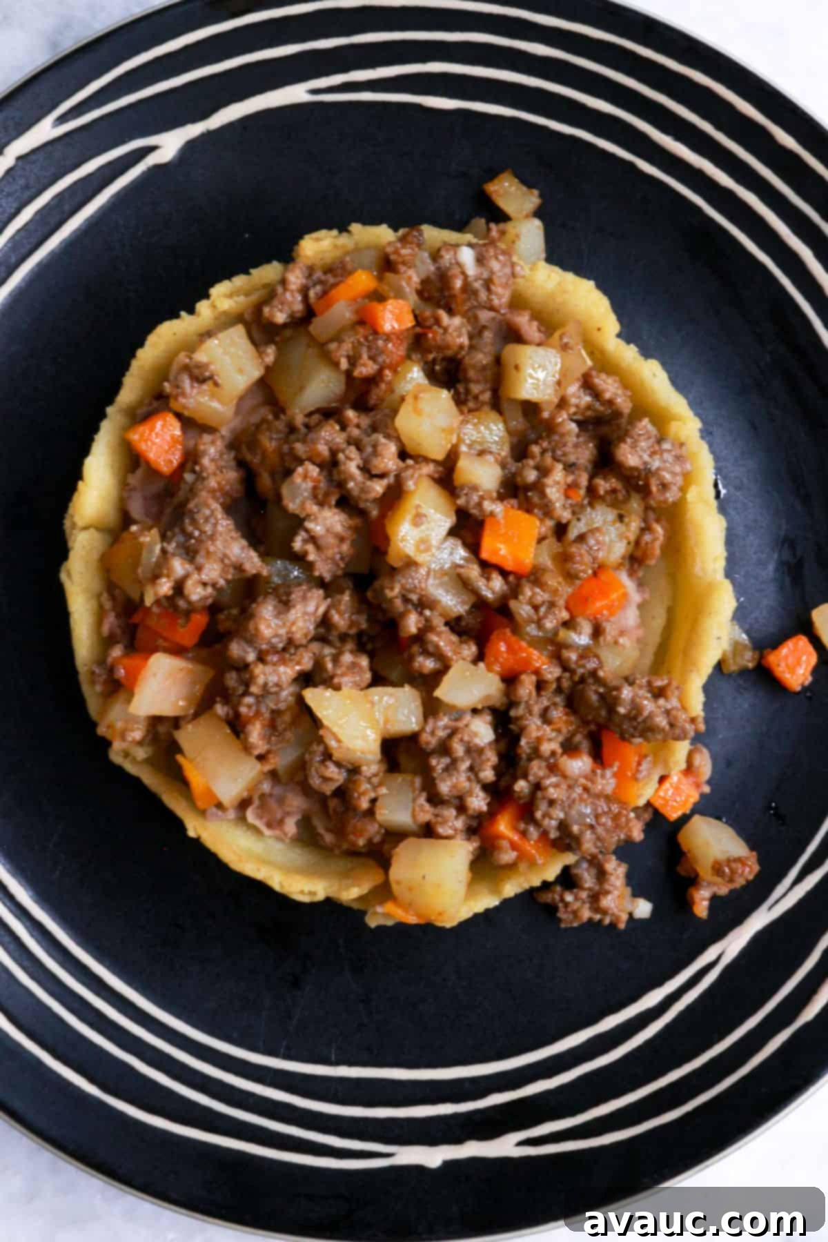 A sope with beans and picadillo on a black plate