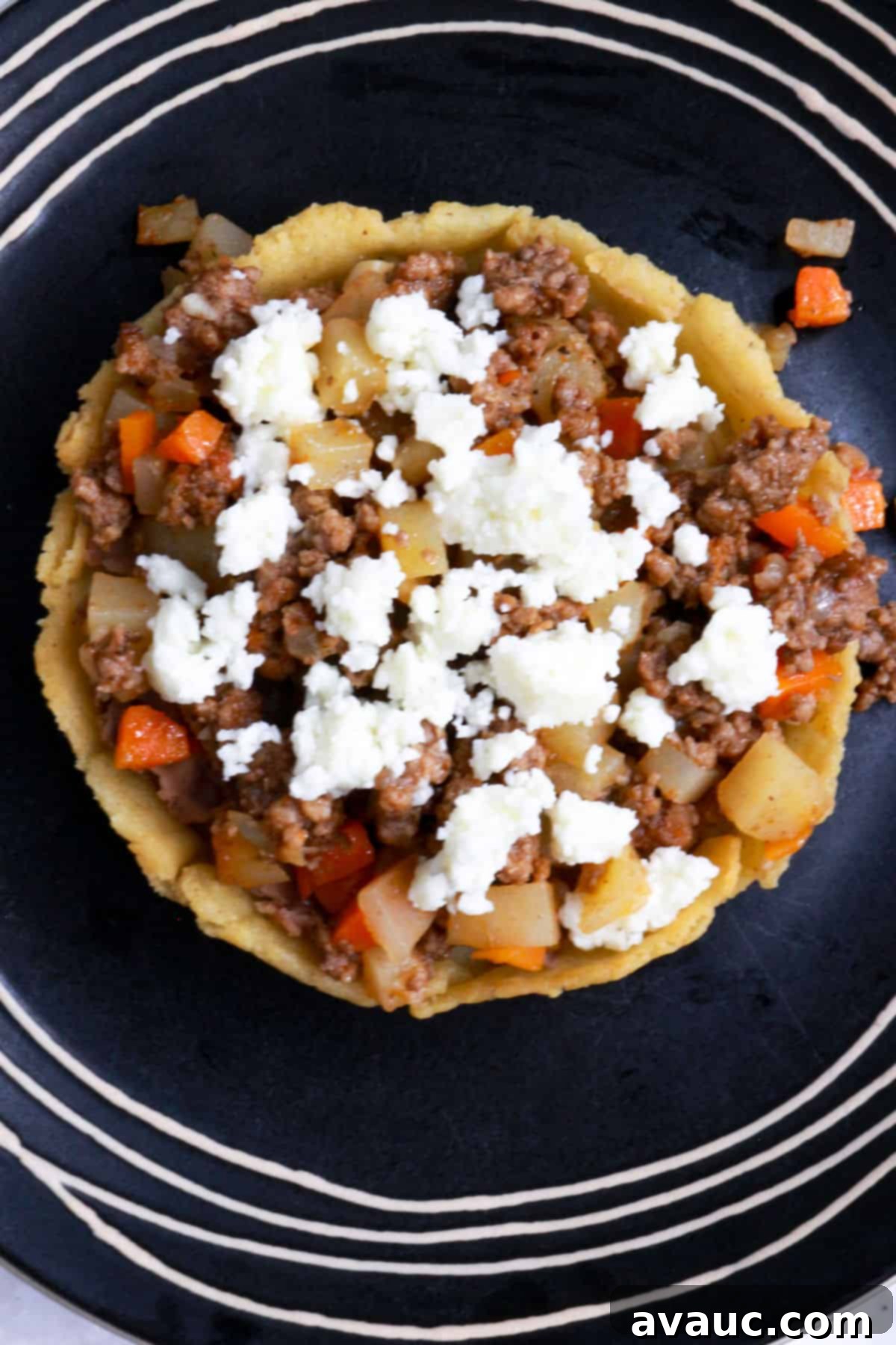 A sope with beans, picadillo and queso fresco on a black plate