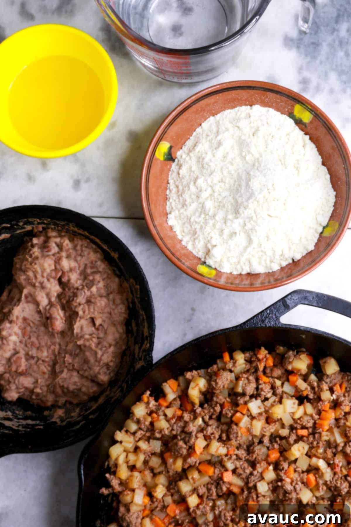 Bowl of oil, bowl of masa marina, measuring cup with water, pan with refried beans, and a pan with picadillo