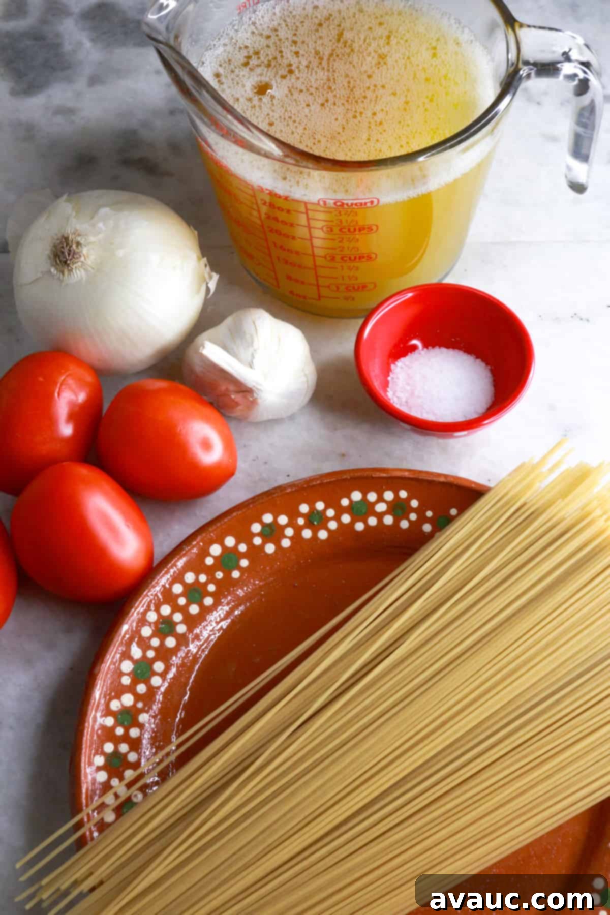 Delicious Gluten-Free Mexican Fideo Soup 3 A measuring cup with chicken broth, a whole onion, 4 tomatoes, a bulb of garlic, a small bowl with salt and a plate with noodles