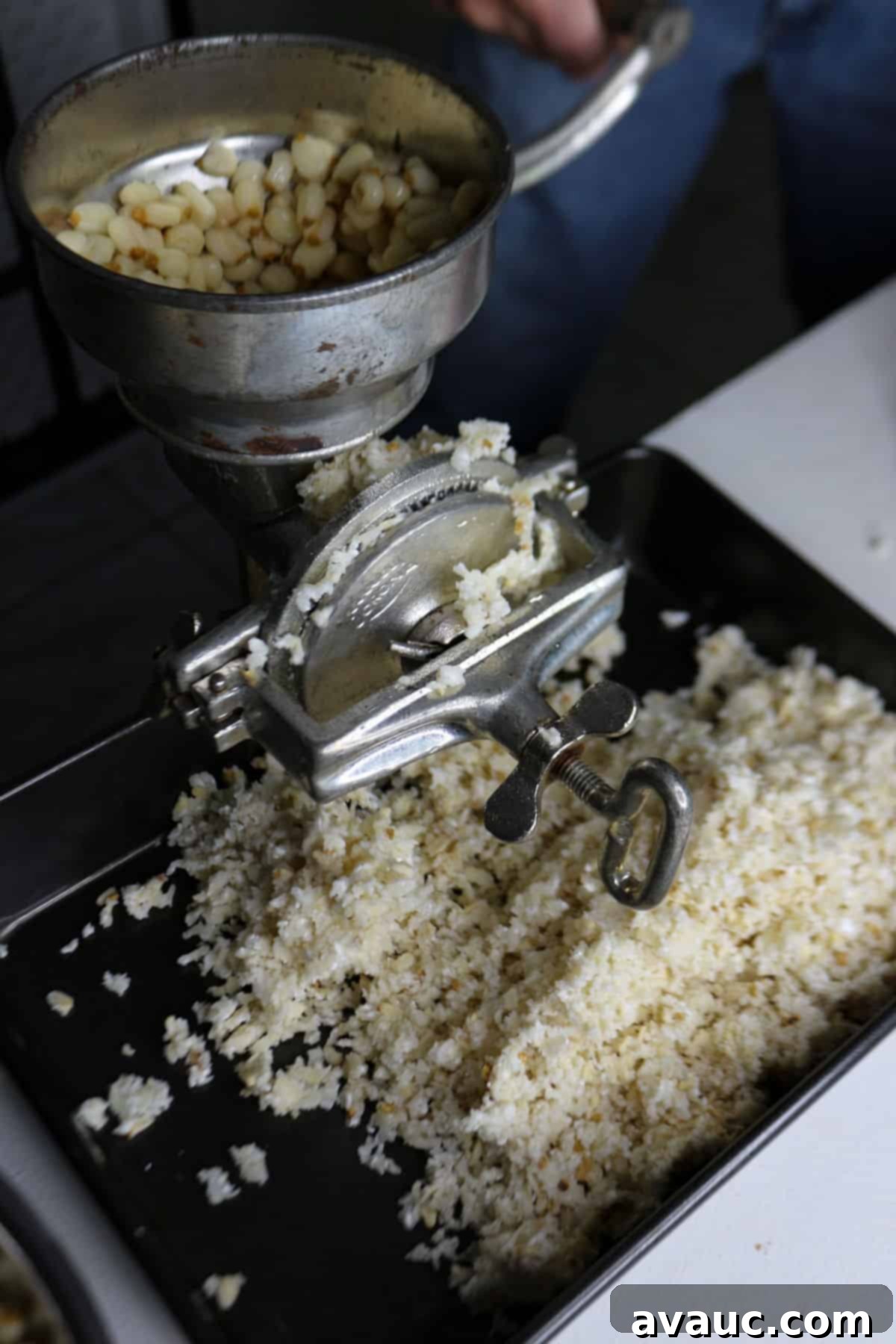 Mastering Nixtamalization for Authentic Tamales 8 Grinding nixtamalized corn using a traditional hand-crank mill to create fresh masa for tamales.
