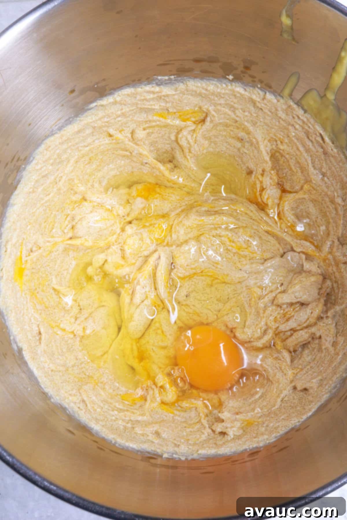 Brown sugar and softened butter being creamed together in a mixing bowl with a hand mixer, with eggs being added.