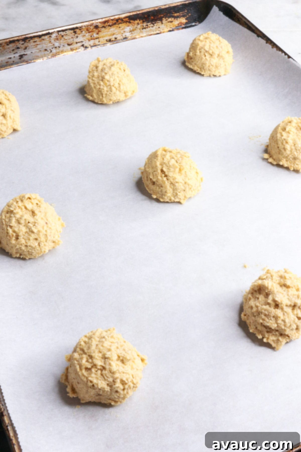 Raw coconut flour oatmeal cookie dough scooped onto a parchment-lined baking sheet, spaced out for baking.