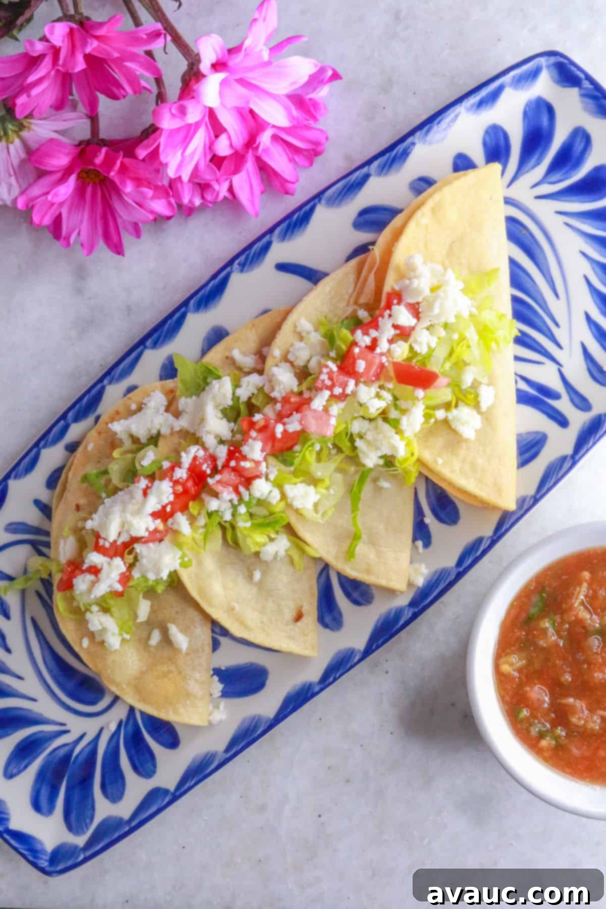 Golden Crispy Bean Tacos 2 Tacos dorados de frijoles in a row on a platter, topped with lettuce, tomatoes and queso fresco