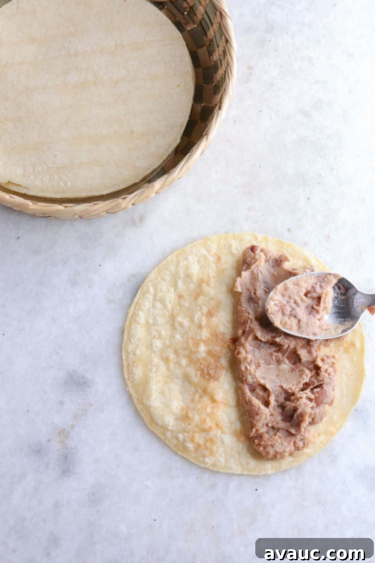 Golden Crispy Bean Tacos 5 Using a spoon to spread refried beans on a warm corn tortilla