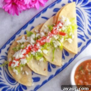 Golden Crispy Bean Tacos 10 Tacos dorados de frijoles in a row on a platter, topped with lettuce, tomatoes and queso fresco