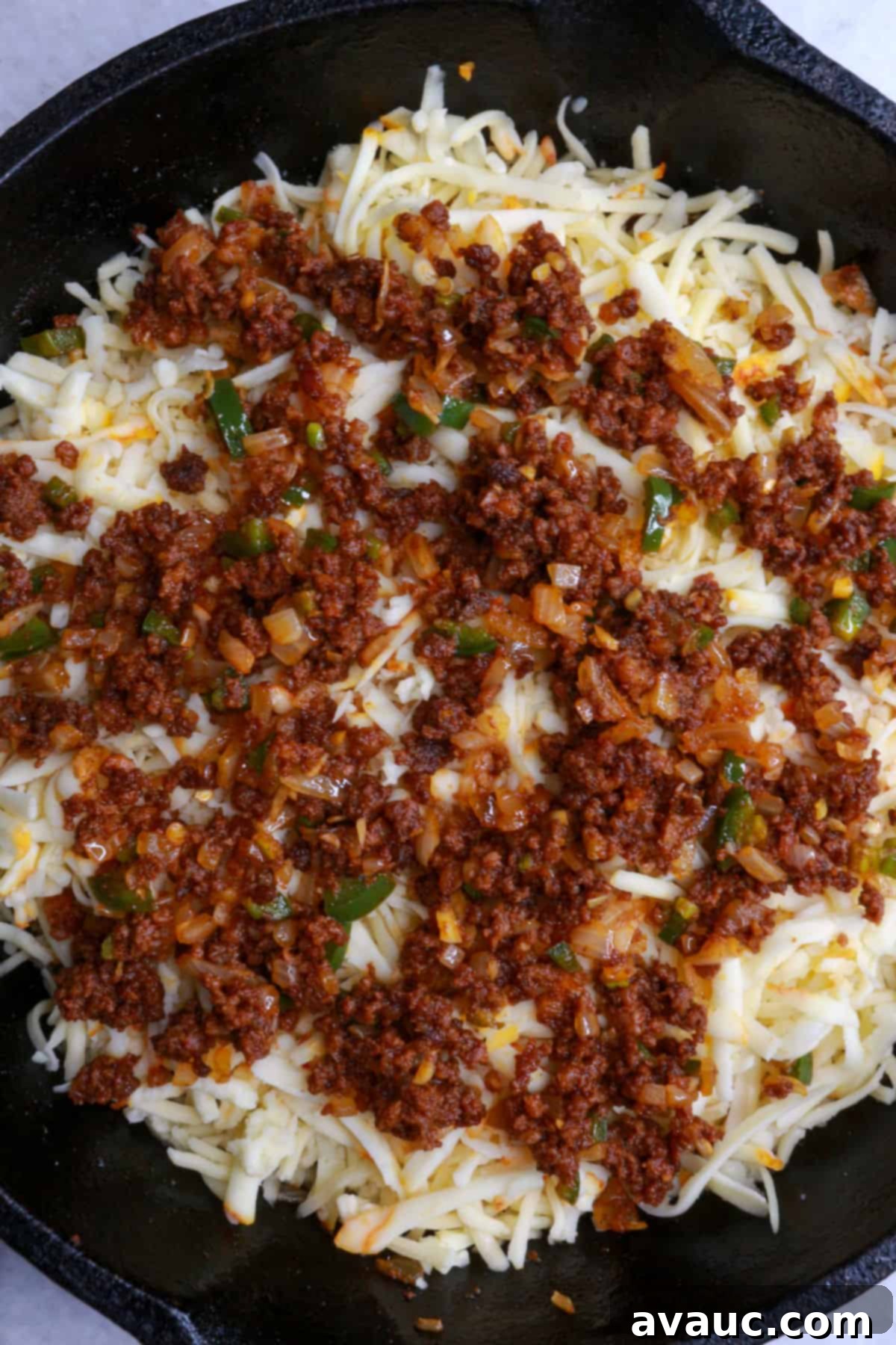 Spicy Chorizo Queso Dip 9 Shredded Mexican cheeses topped with a layer of the reserved chorizo and veggie mixture in a cast-iron skillet, poised for baking.