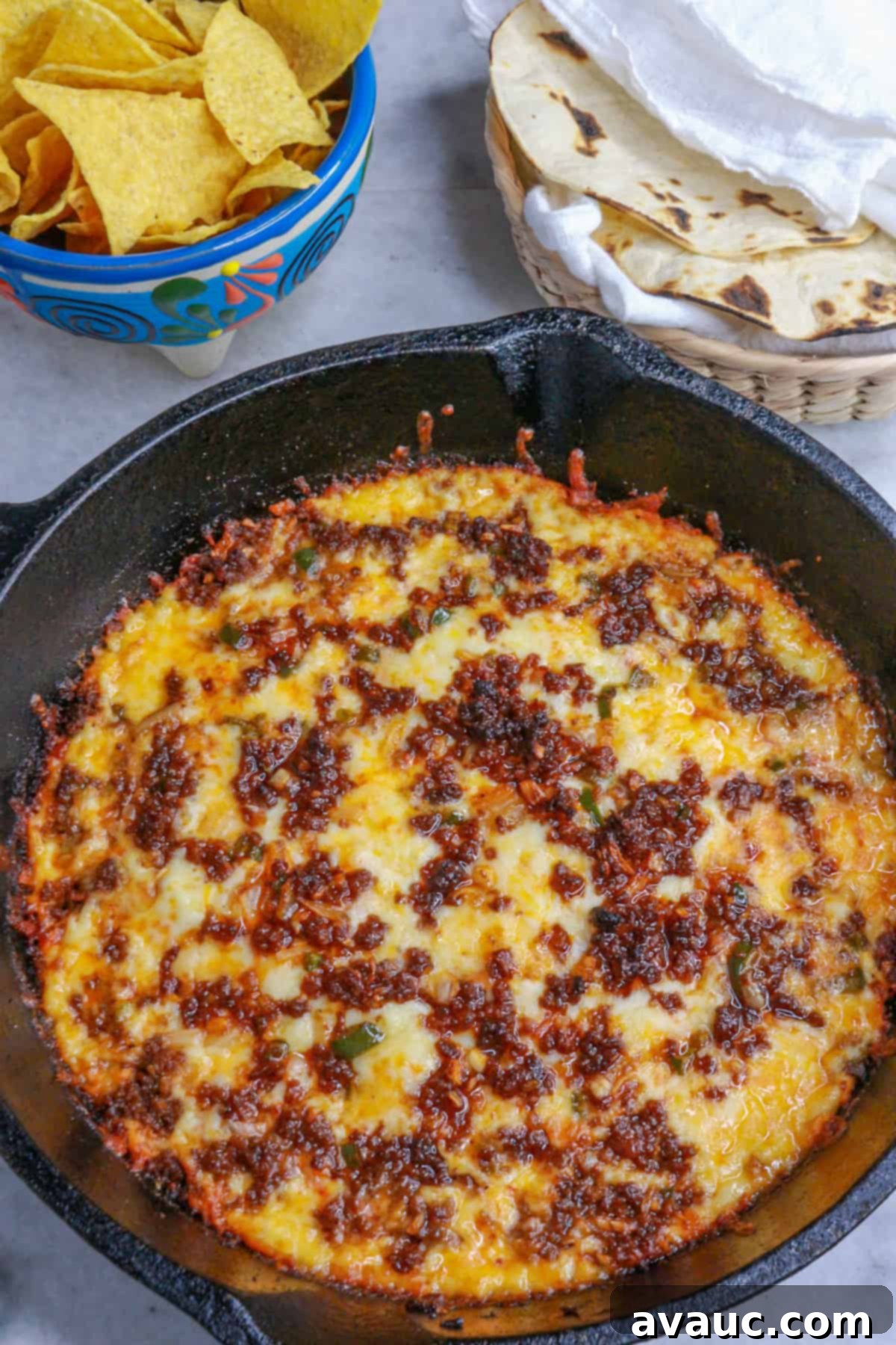 Spicy Chorizo Queso Dip 2 Cast-iron skillet with bubbling choriqueso, a bowl of crispy tortilla chips, and a basket of warm corn tortillas behind it, ready to serve.