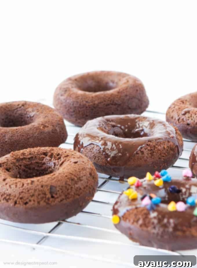 Cosmic Triple Chocolate Cake Donuts on wire rack with rainbow sprinkles and chocolate ganache glaze