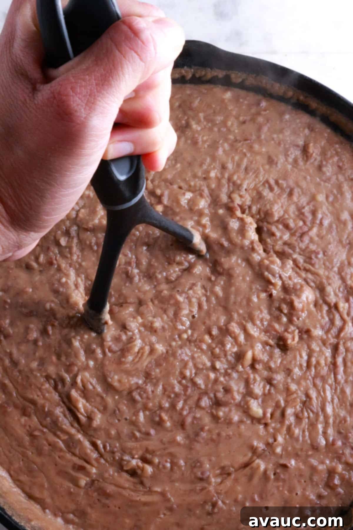 Classic Refried Bean Sopes 4 A hand on a potato masher mashing beans in a cast-iron skillet