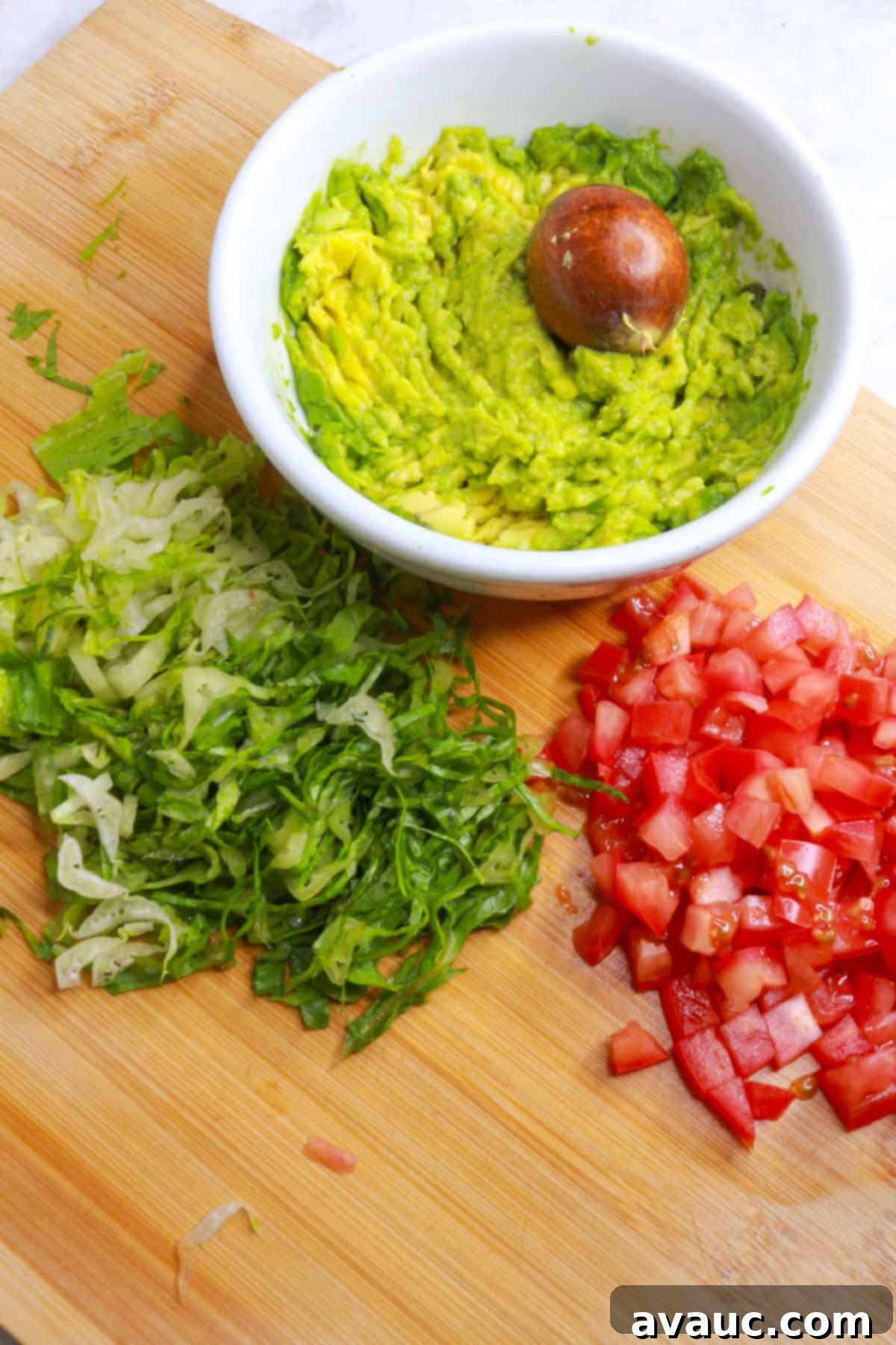Classic Refried Bean Sopes 5 A bowl with mashed avocado on a cutting board with shredded lettuce and diced tomato