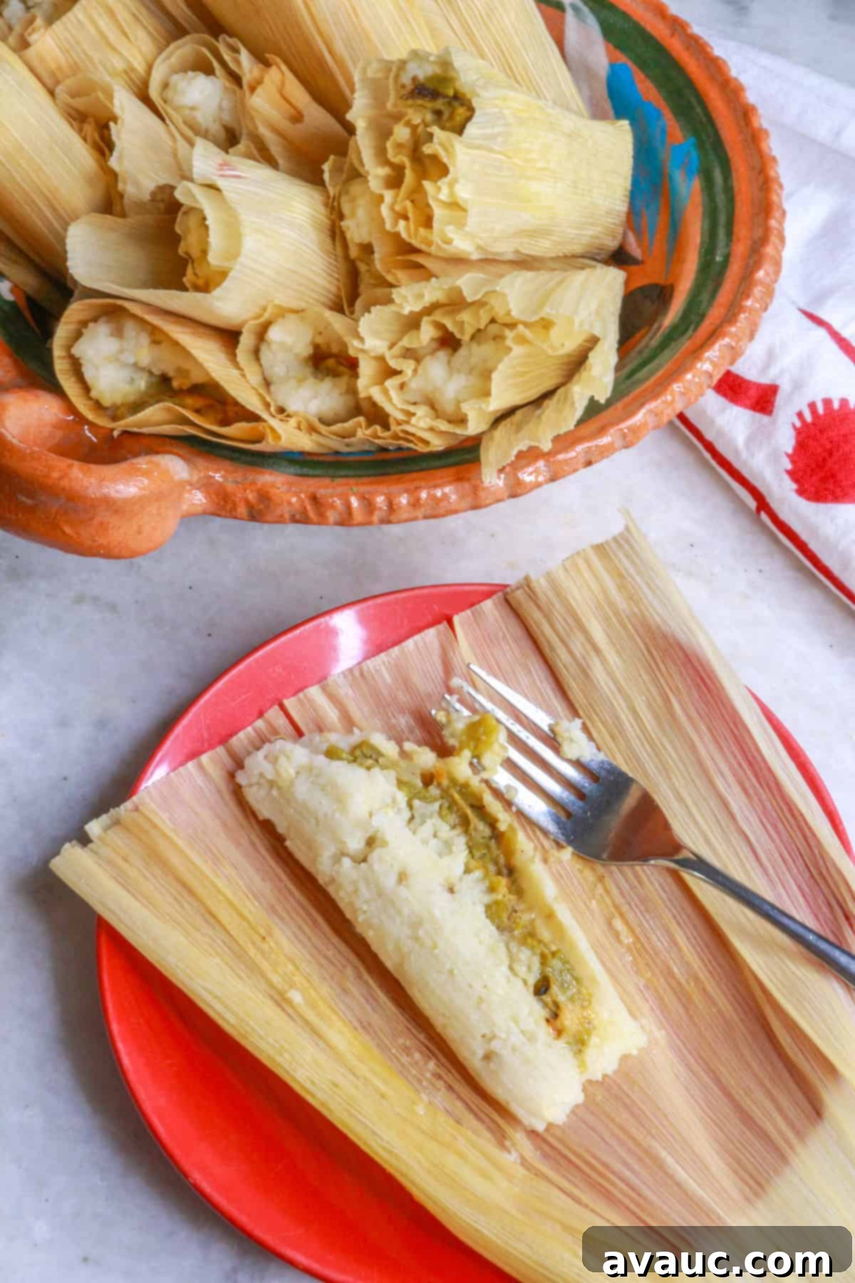 Top view of an open green chile and cheese tamal on a plate with a bowl of tamales behind it