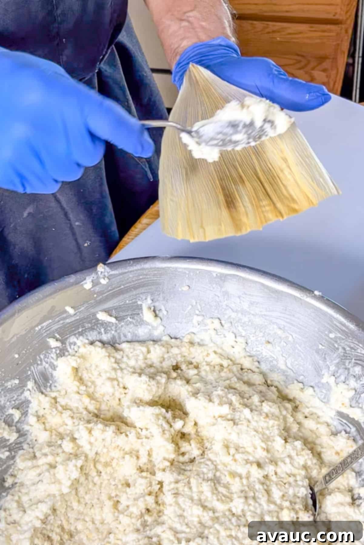 Holding a corn husk and about to spread masa on it
