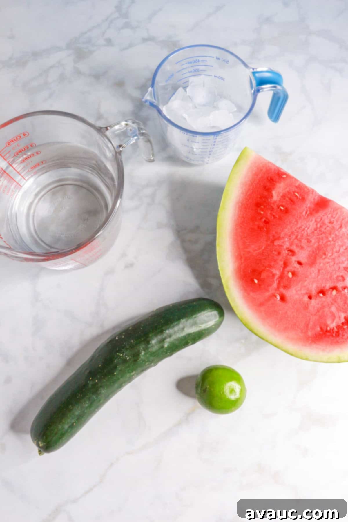 Vibrant Cucumber Watermelon Cooler 3 A selection of fresh ingredients for cucumber watermelon agua fresca: a measuring cup filled with ice, another with filtered water, a large wedge of ripe watermelon, a whole cucumber, and a fresh lime.
