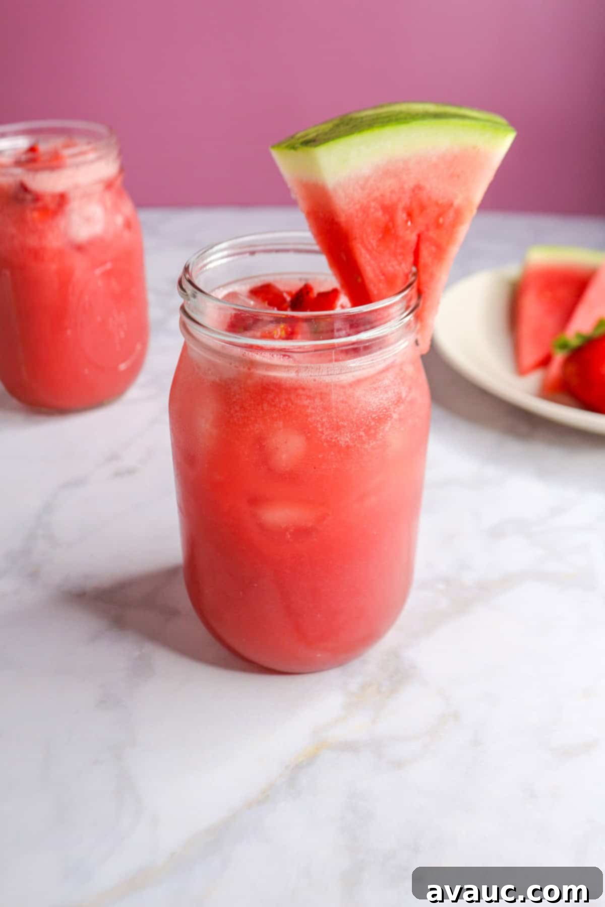 Watermelon Strawberry Agua Fresca 10 Two glasses of vibrant Watermelon Strawberry Agua Fresca, one garnished with a watermelon slice and the other full, set against a blurred background.